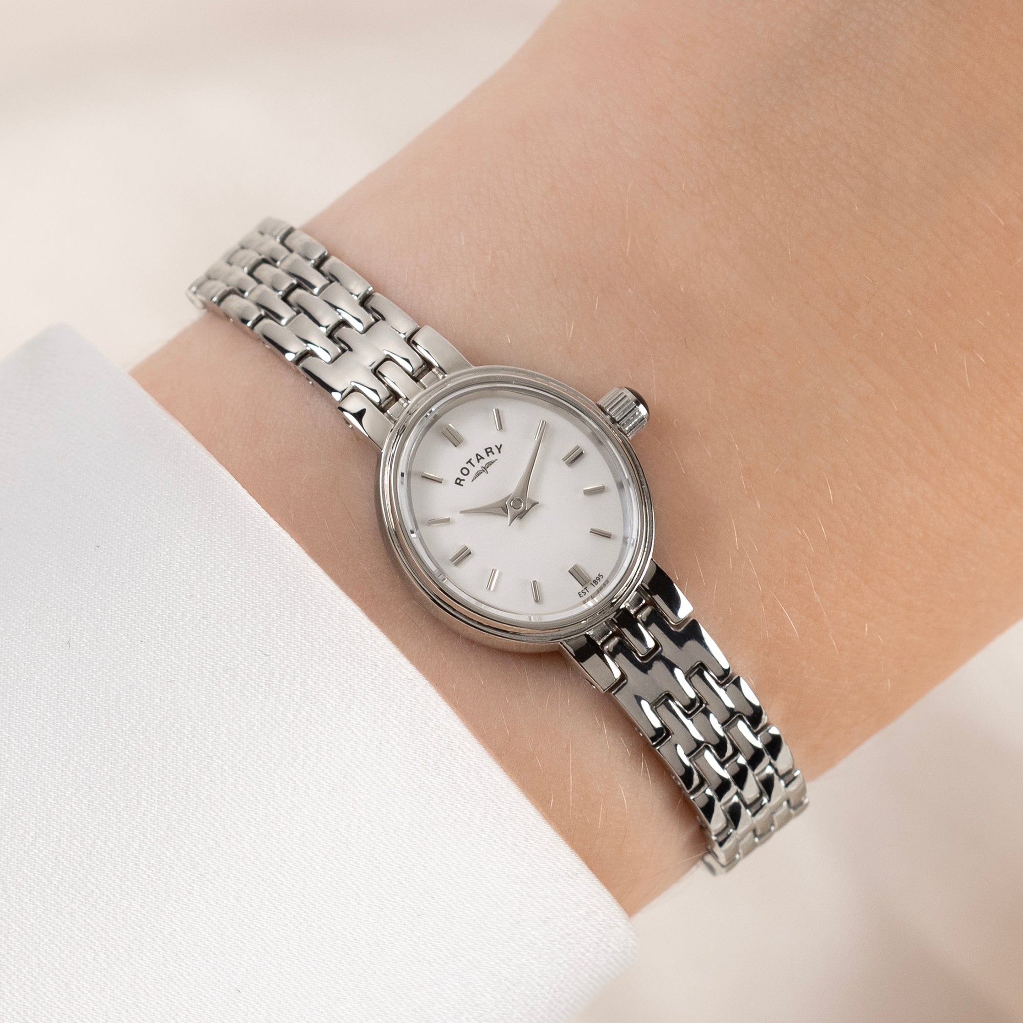 Silver Rotary watch with a white face on a wrist against a light background