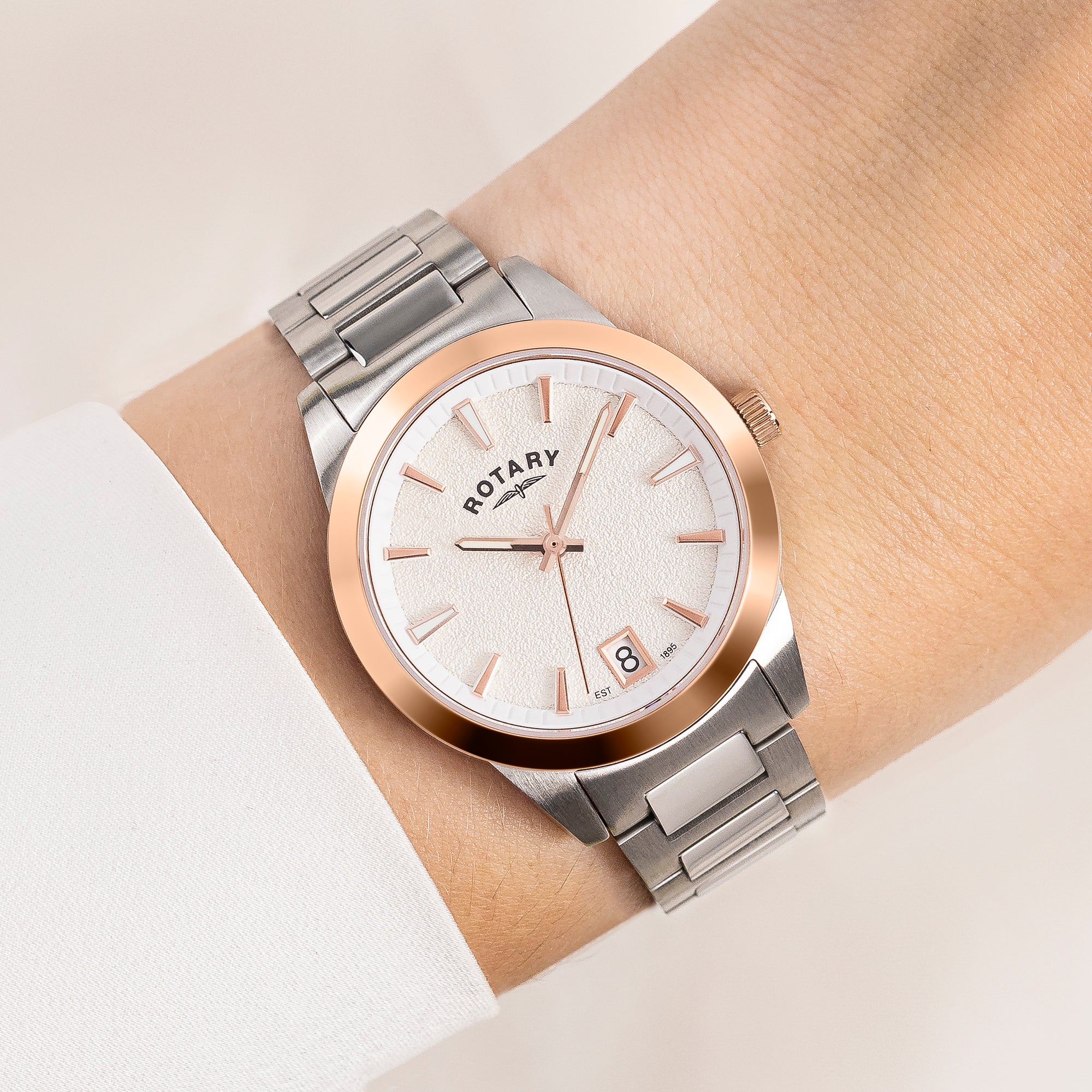 Silver and rose gold Rotary watch on a wrist with a light background