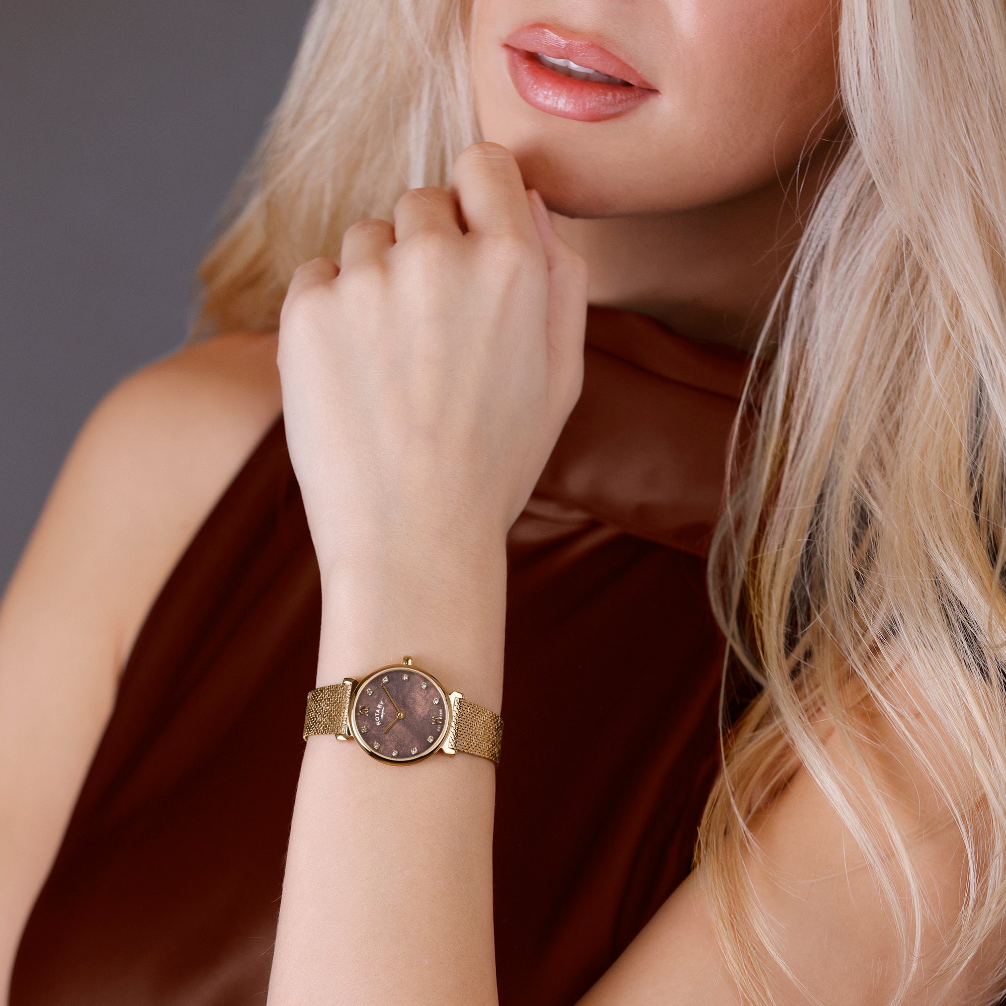 Woman wearing a Rotary 1895 rose gold watch with a dark face on a neutral background