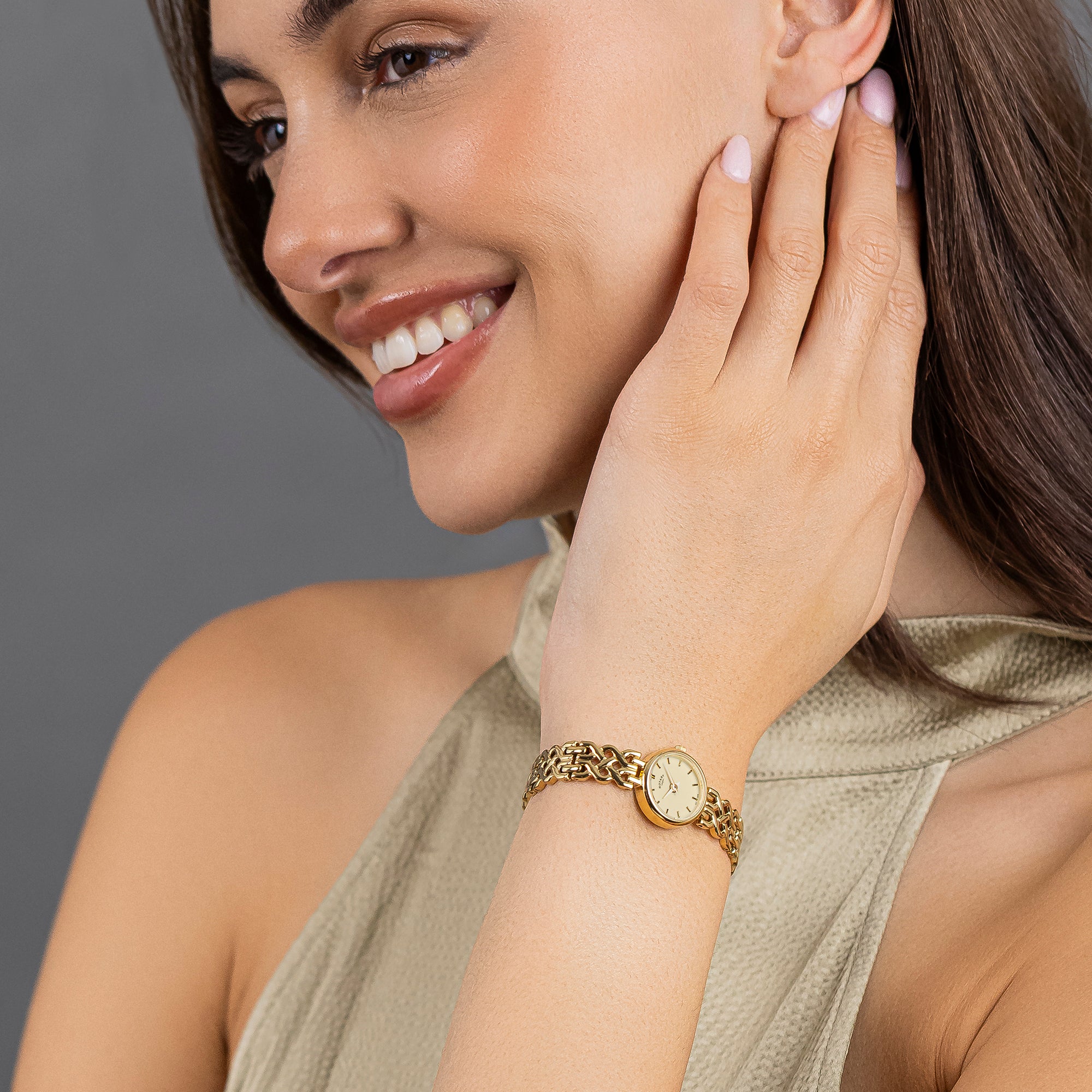 Woman wearing a gold Rotary 1895 bracelet with a watch face design on a gray background