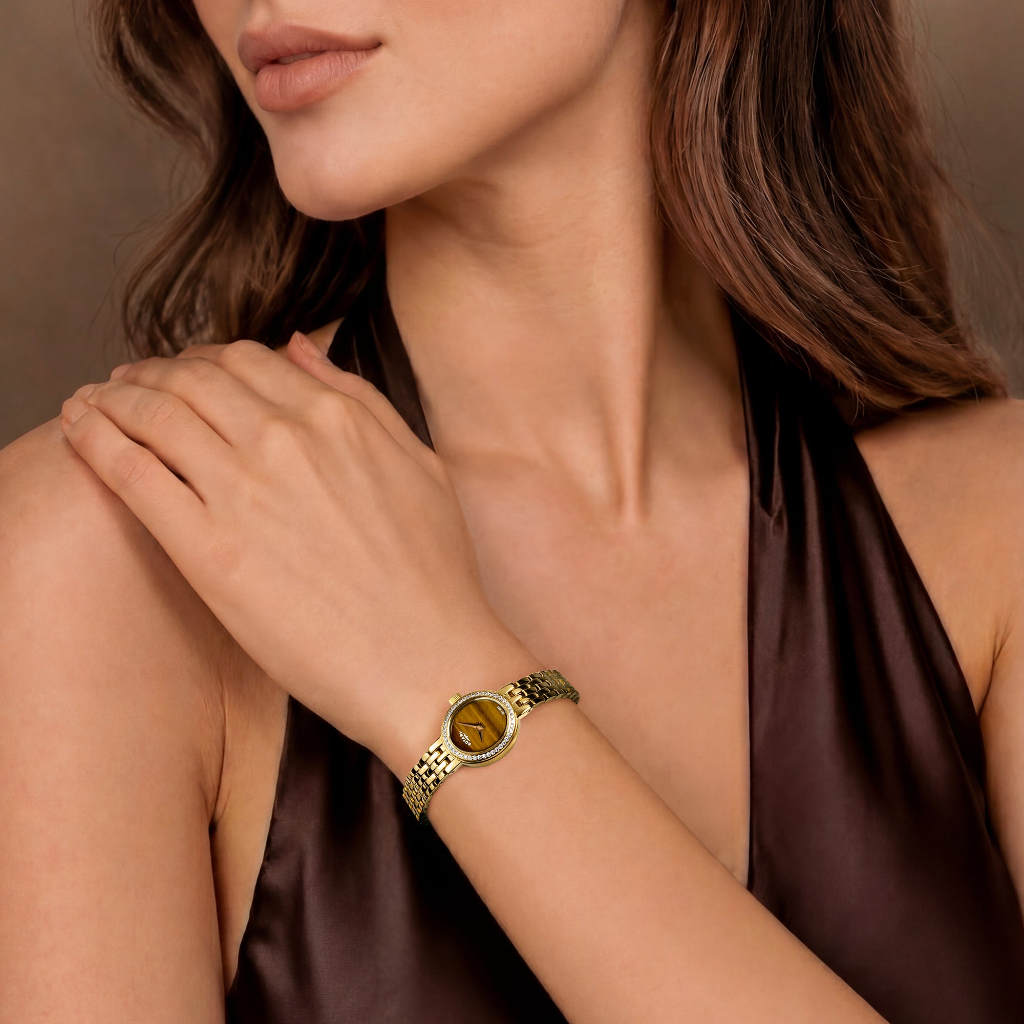 Woman wearing a gold Rotary cocktail bracelet watch with a brown background