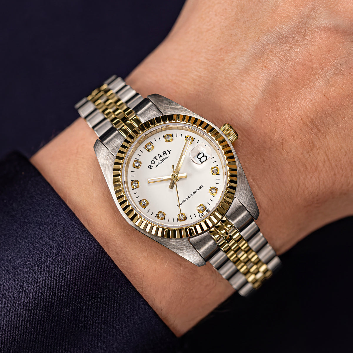 A two-tone Rotary stainless steel and gold wristwatch with a white dial, worn on a ladies wrist against a dark navy background.