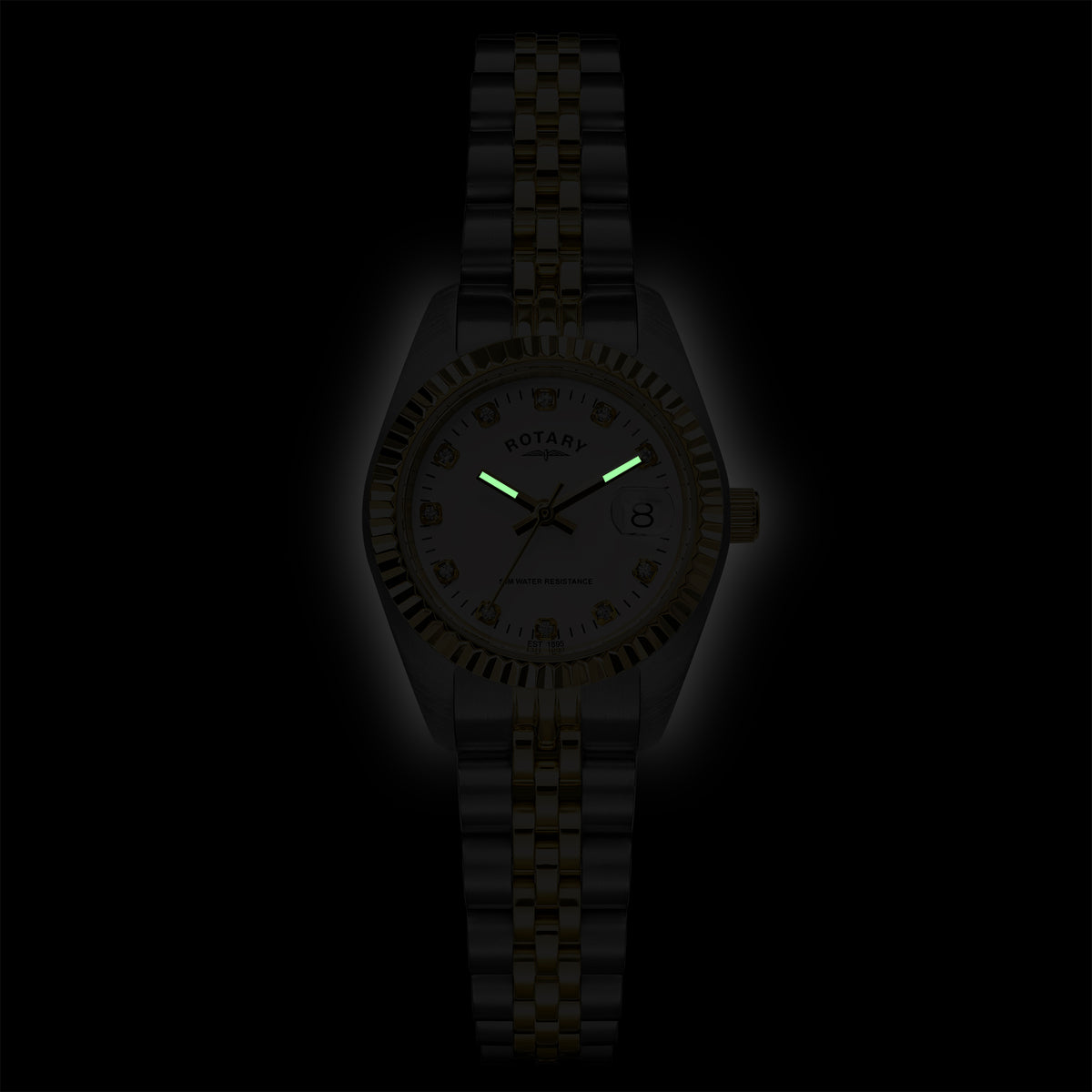 A Rotary wristwatch with a metallic link bracelet and a white dial, shown against a black background. The watch hands and markers glow green in the dark, and the brand name 'ROTARY' is visible on the dial.
