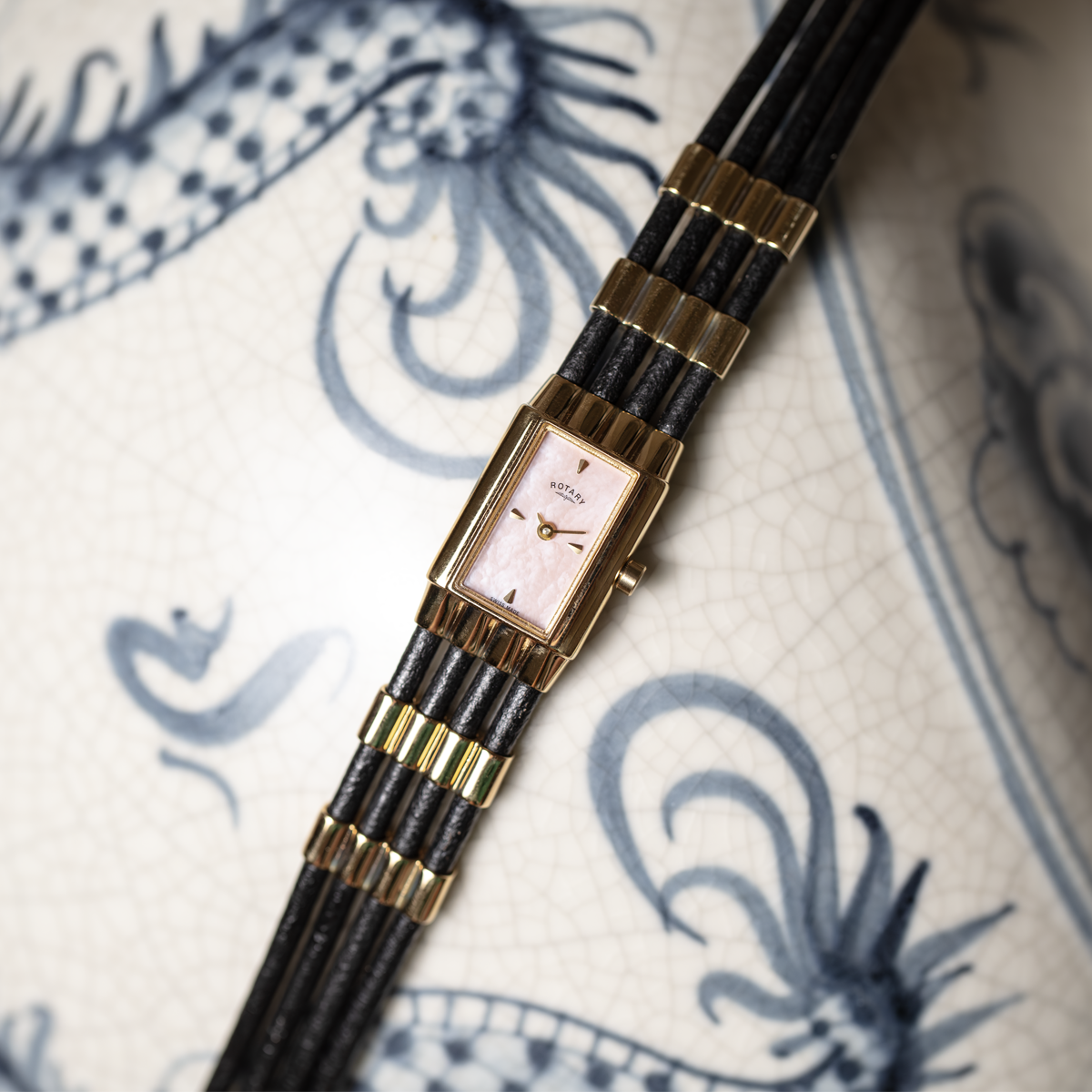 Vintage-style watch with gold and black strap on a decorative fabric background