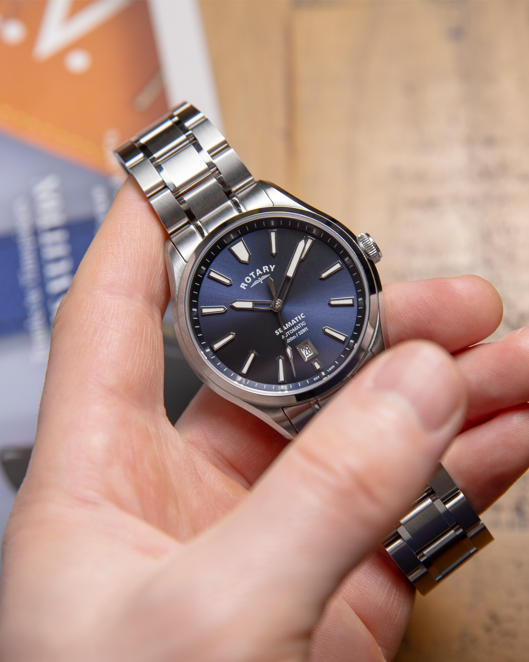 Hand holding a silver Rotary Seamatic 100 wristwatch with a blue face on a blurred background