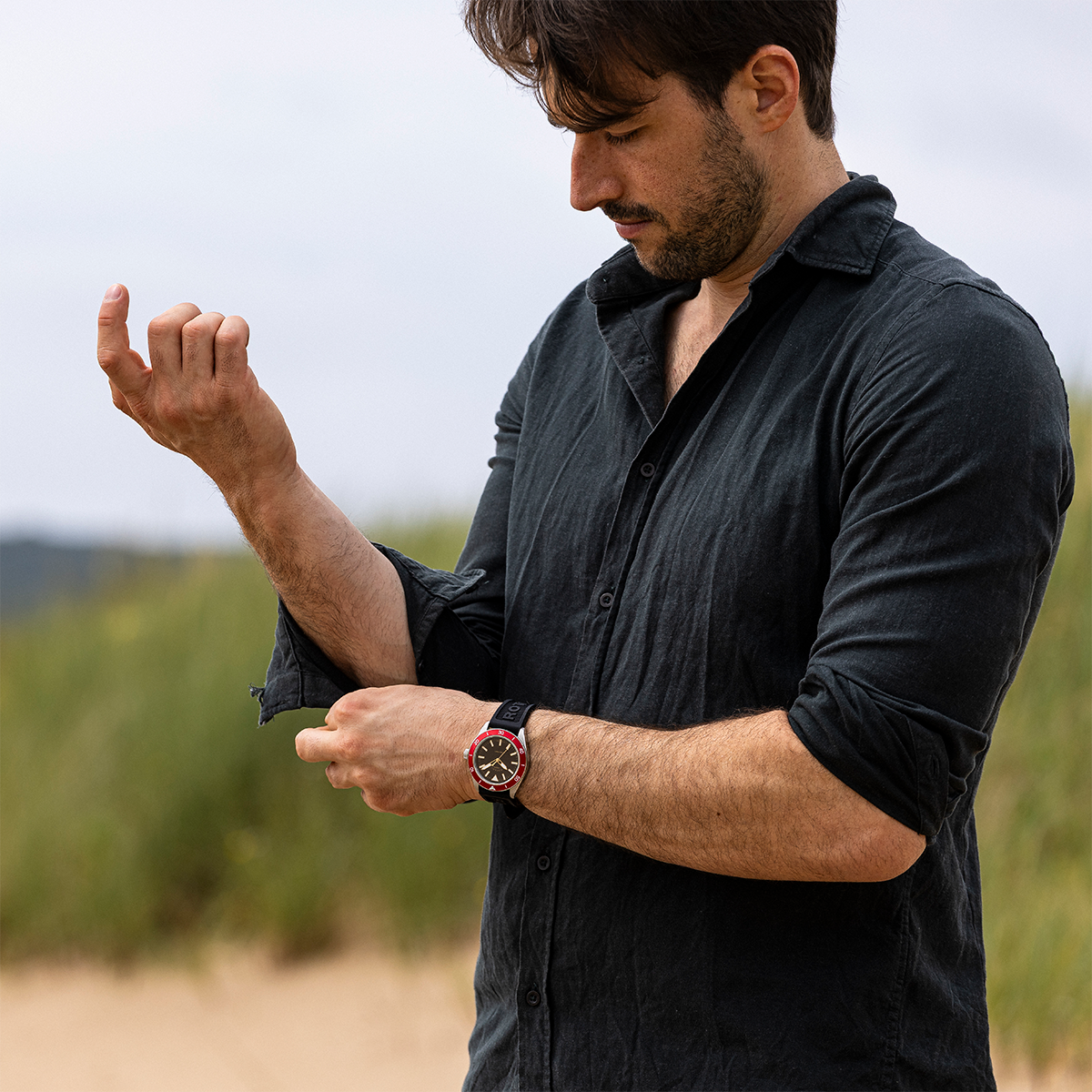 Man wearing a black shirt and Rotary Apex100 watch on a beach