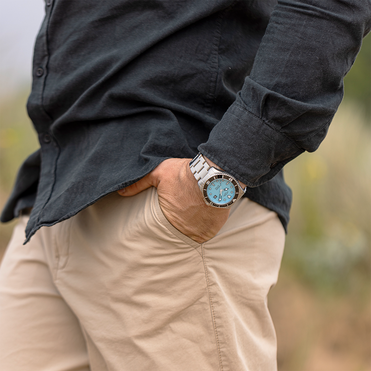 Person wearing a dark shirt and beige pants with a Rotary Seamatic watch on a blurred natural background