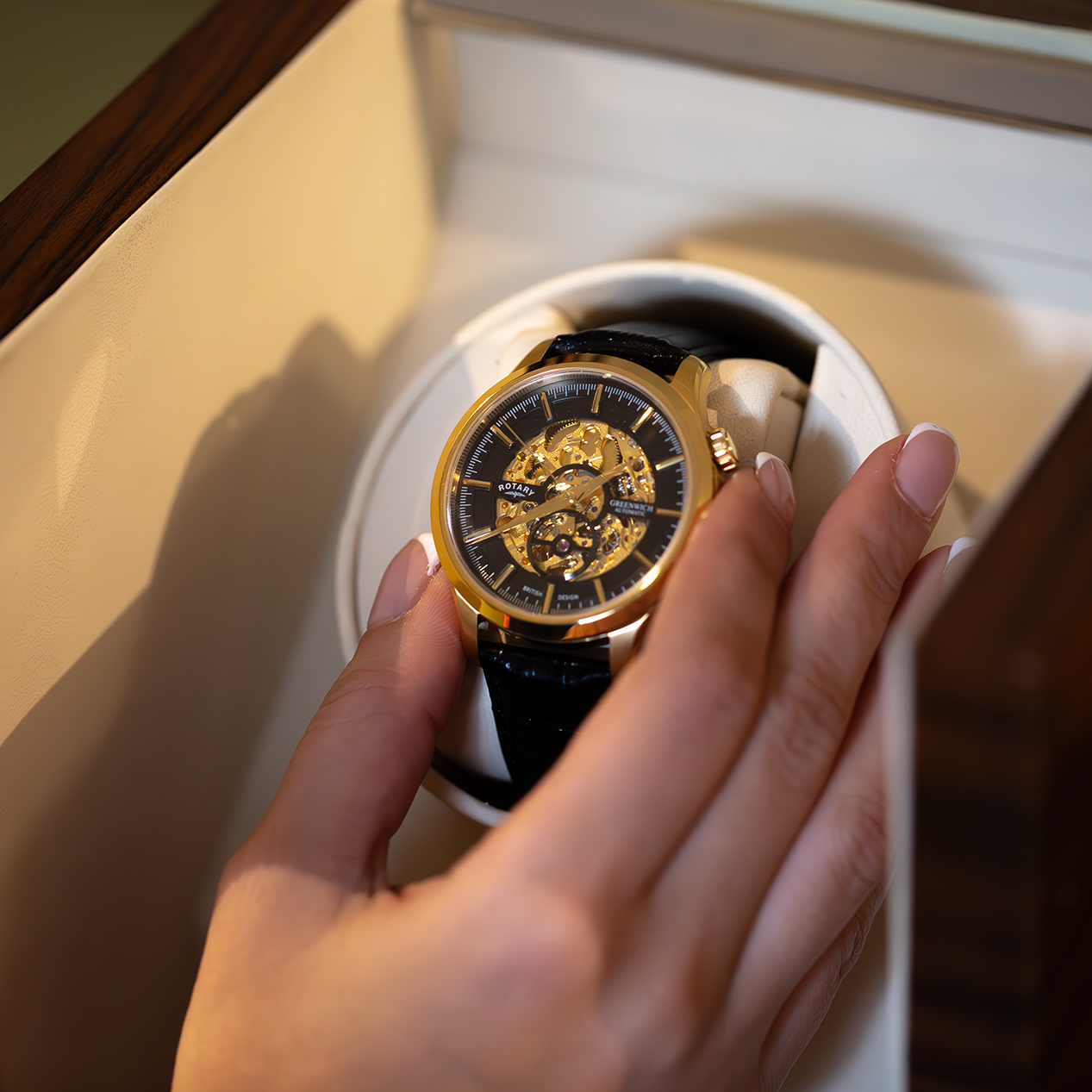 A gold rotary watch being put into a watch winder by a woman