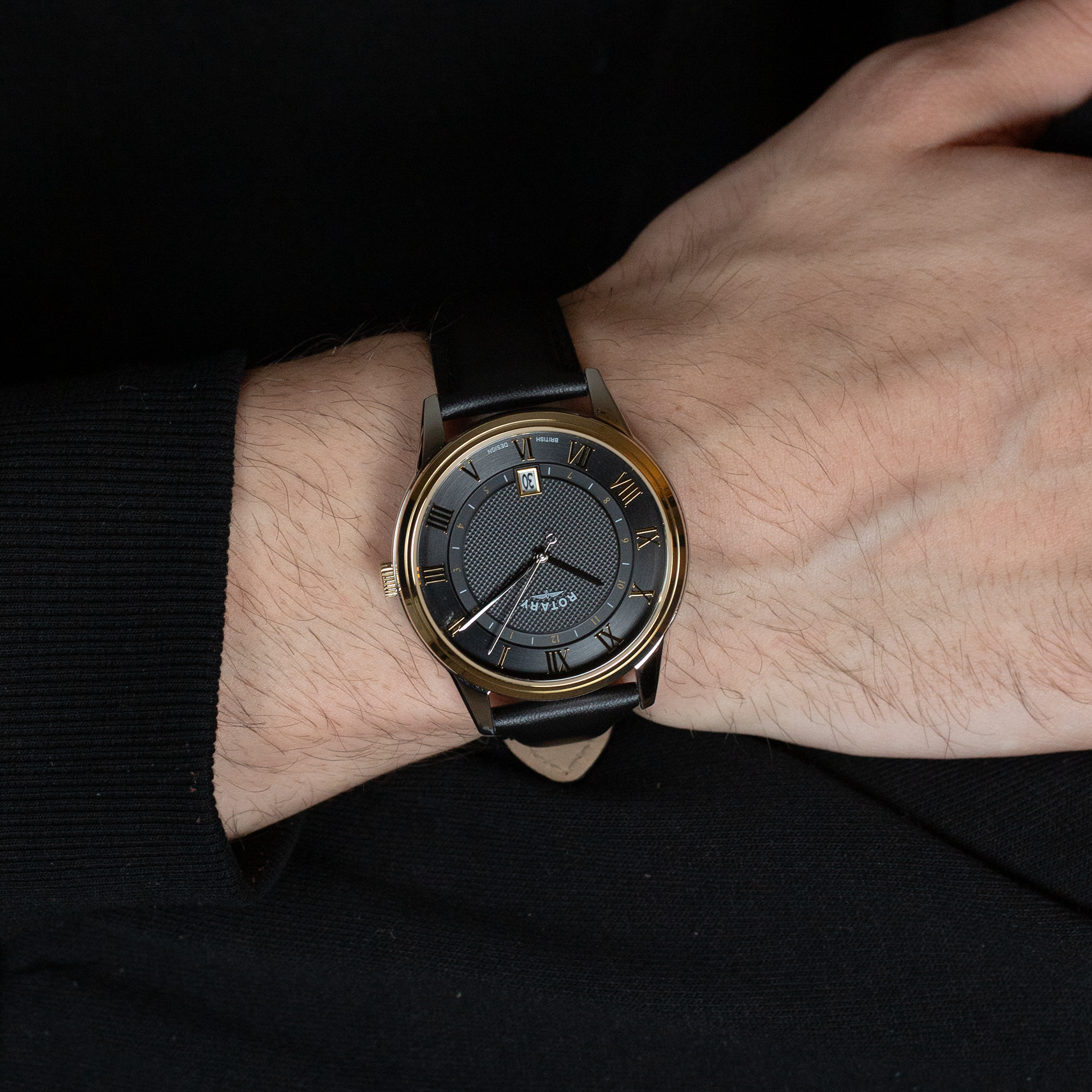 A man wearing a rotary mens watch in two tone with a black leather strap and black dial with gold roman numerals