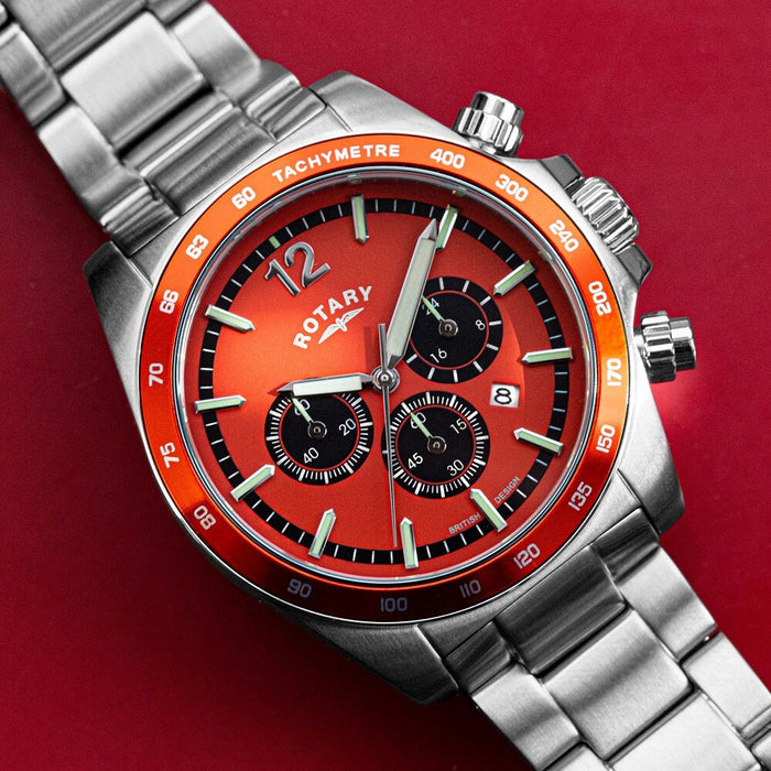 A rotary chronograph watch with a stainless steel case and bracelet, an orange case and an orange bezel. The dial features 3 black sub-dials and a date window, as well as luminescent hands and indexes