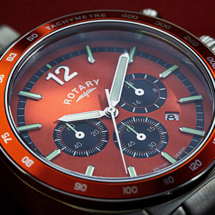 a close up of a Rotary chronograph watch with an orange dial, luminescent hands and 3 sub-dials. There is also an orange bezel with a tachymetre and a date window on the dial