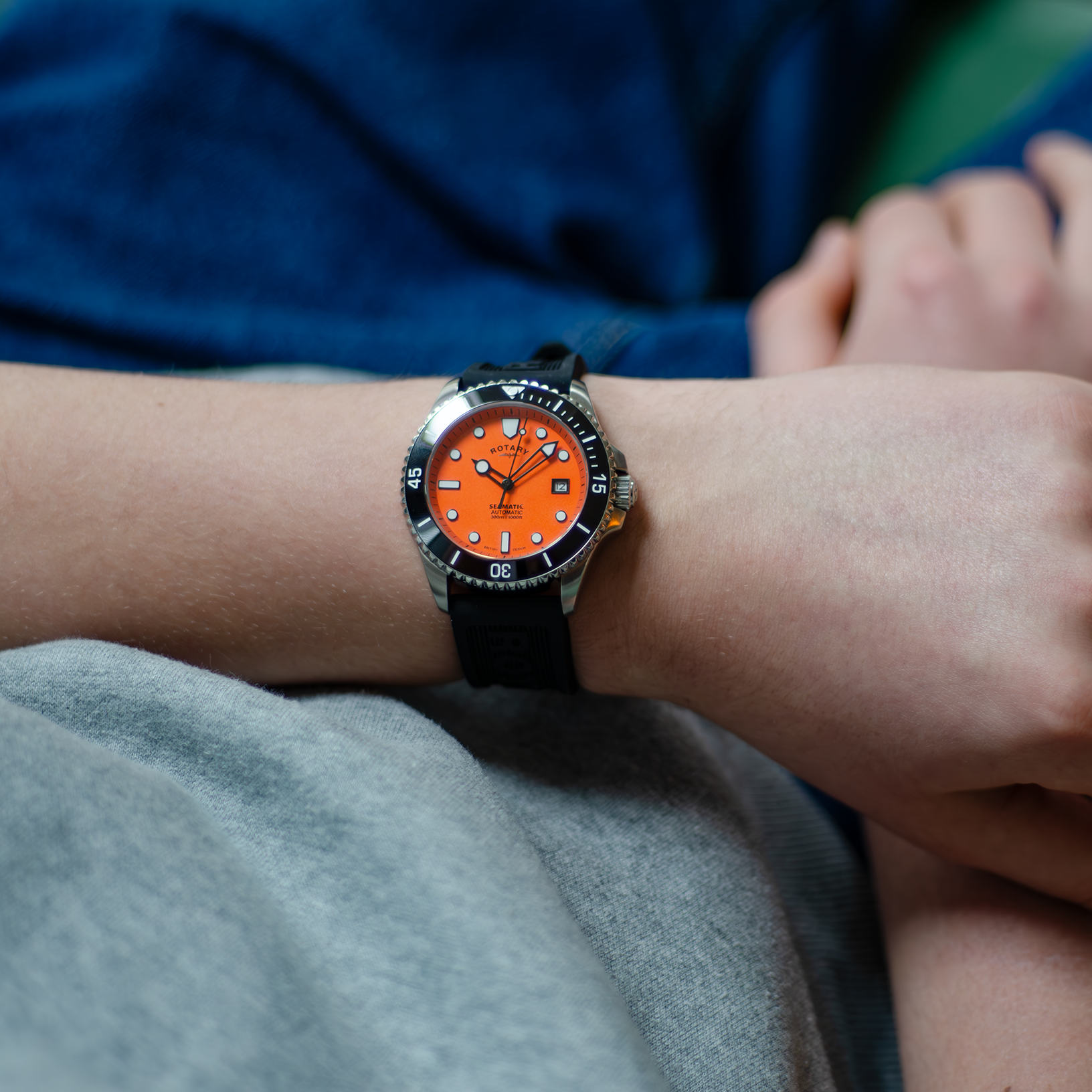 A man wearing a rotary dive watch in stainless steel with an orange dial and a silicone black strap