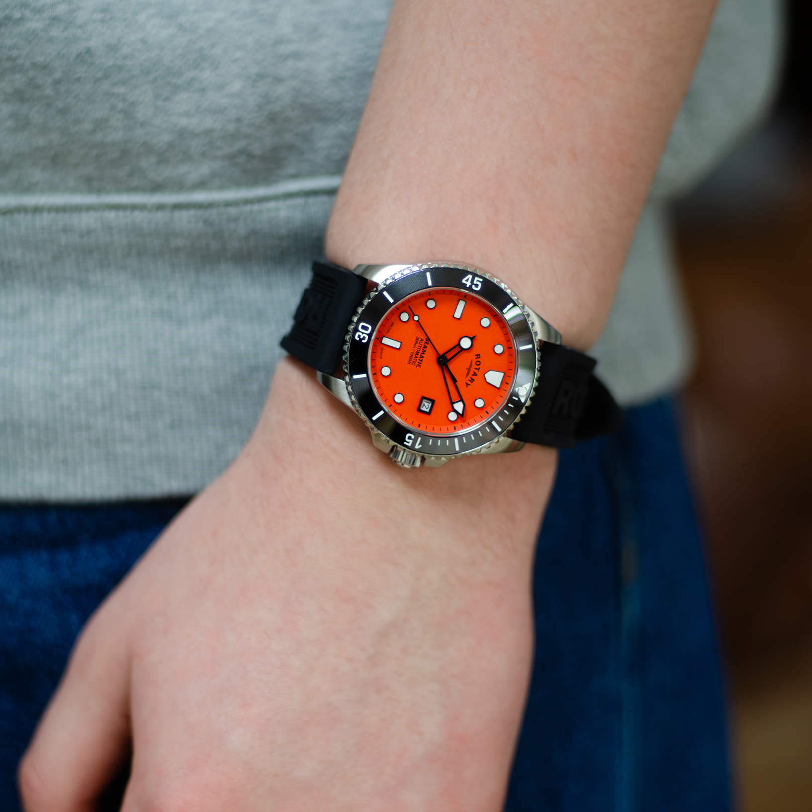 A man wearing a rotary dive watch in stainless steel with an orange dial and a silicone black strap