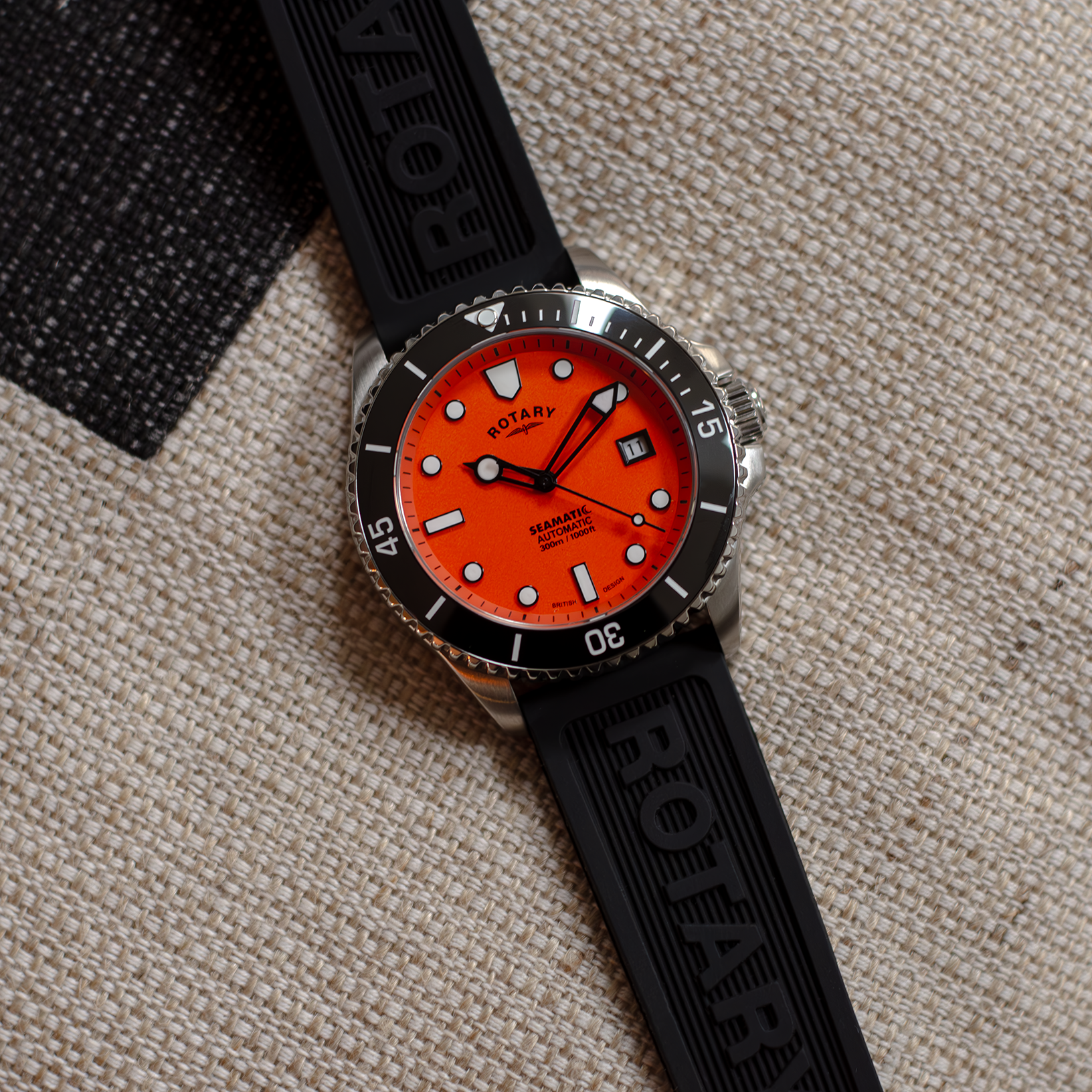 Rotary dive watch with a stainless steel case and orange dial. Pictured against a textured background