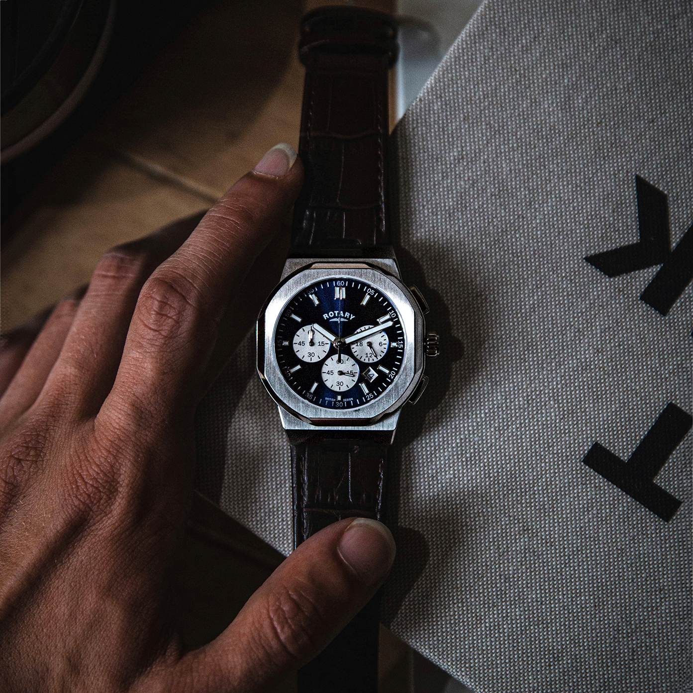 Rotary Regent Chronograph watch on a table with a man holding the leather straps 