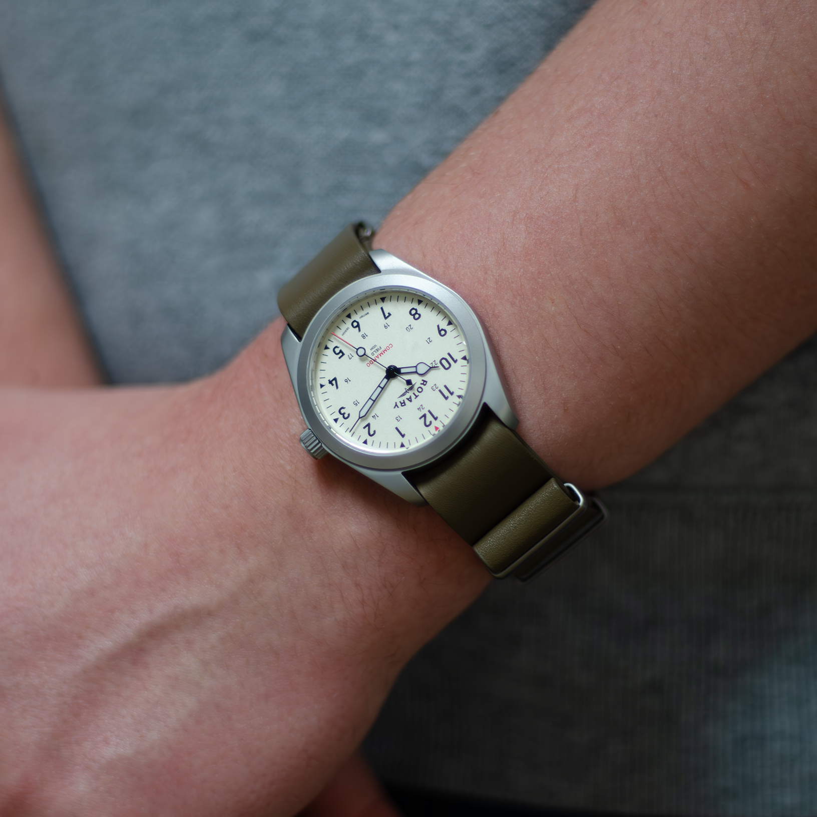 A man dressed in a casual manner wearing a rotary mens watch in stainless steel with a green leather nato strap