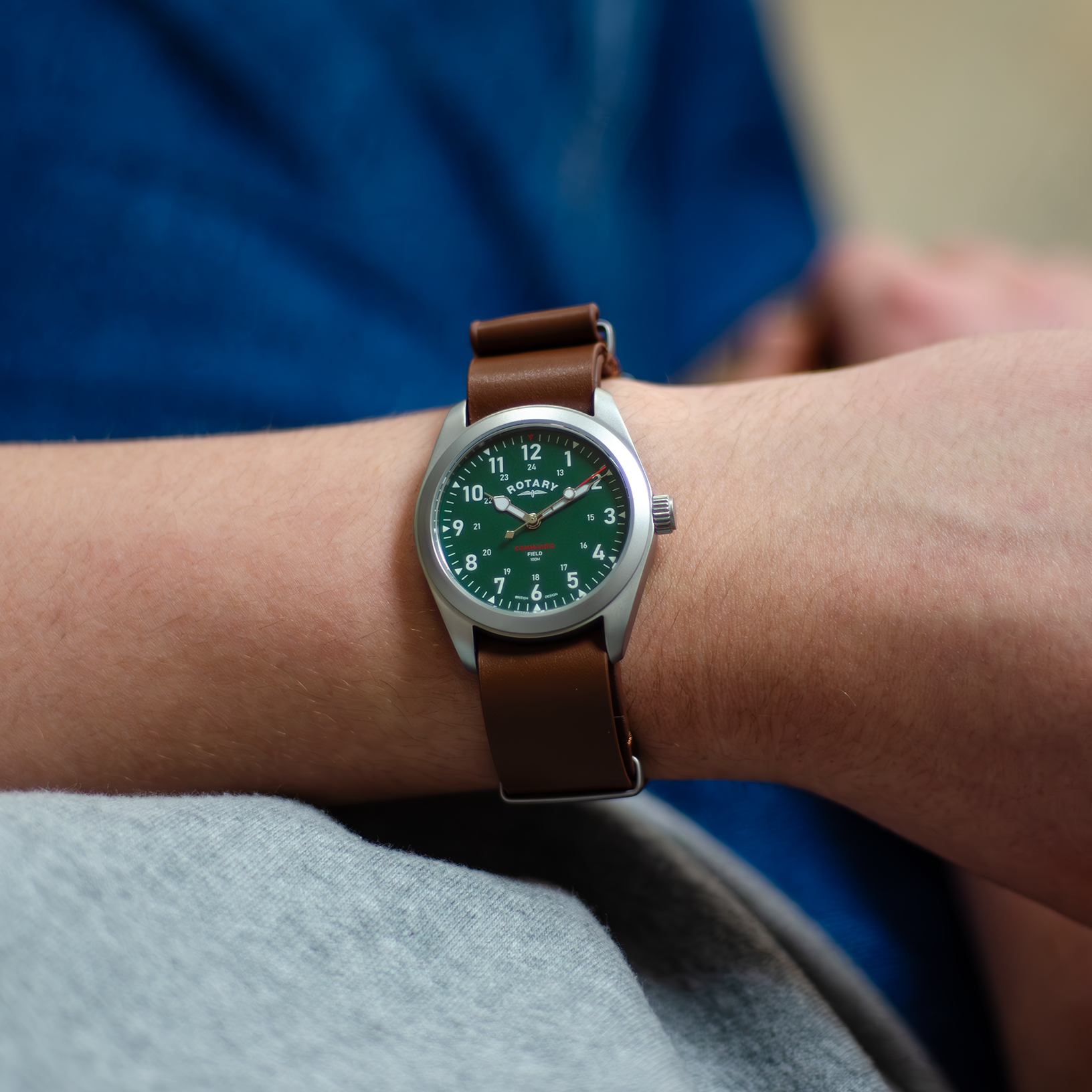 A man dressed in a casual manner wearing a rotary mens watch in stainless steel with a brown leather nato strap