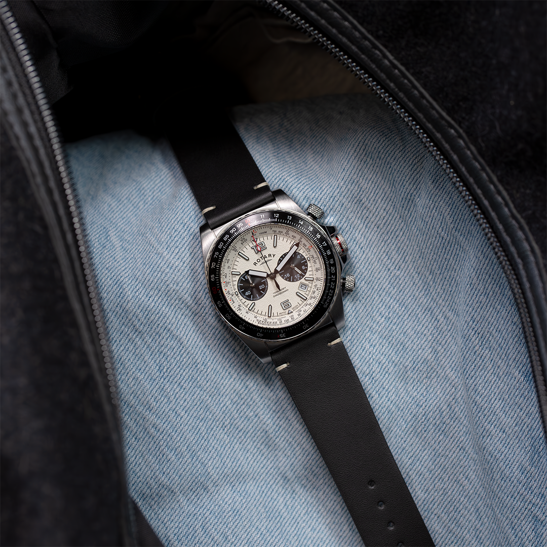 Rotary Aeromaster pilot chronograph watch with a stainless steel case, a cream dial and a black slide rule bezel. The watch is in a black traveling bag with some luggage and sitting on a pair of jeans