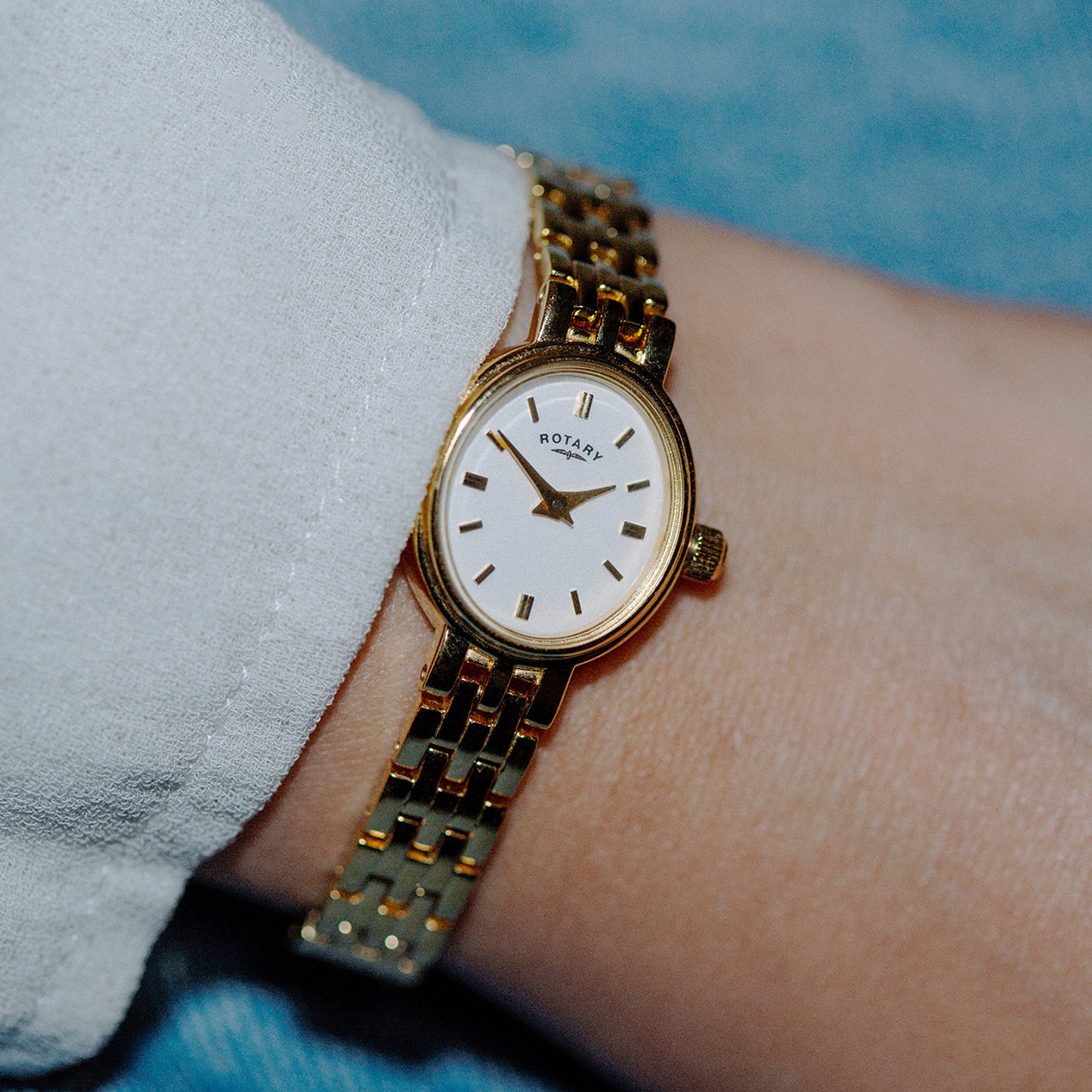 Rotary ladies watch in gold with a bracelet being worn by a woman with a white shirt