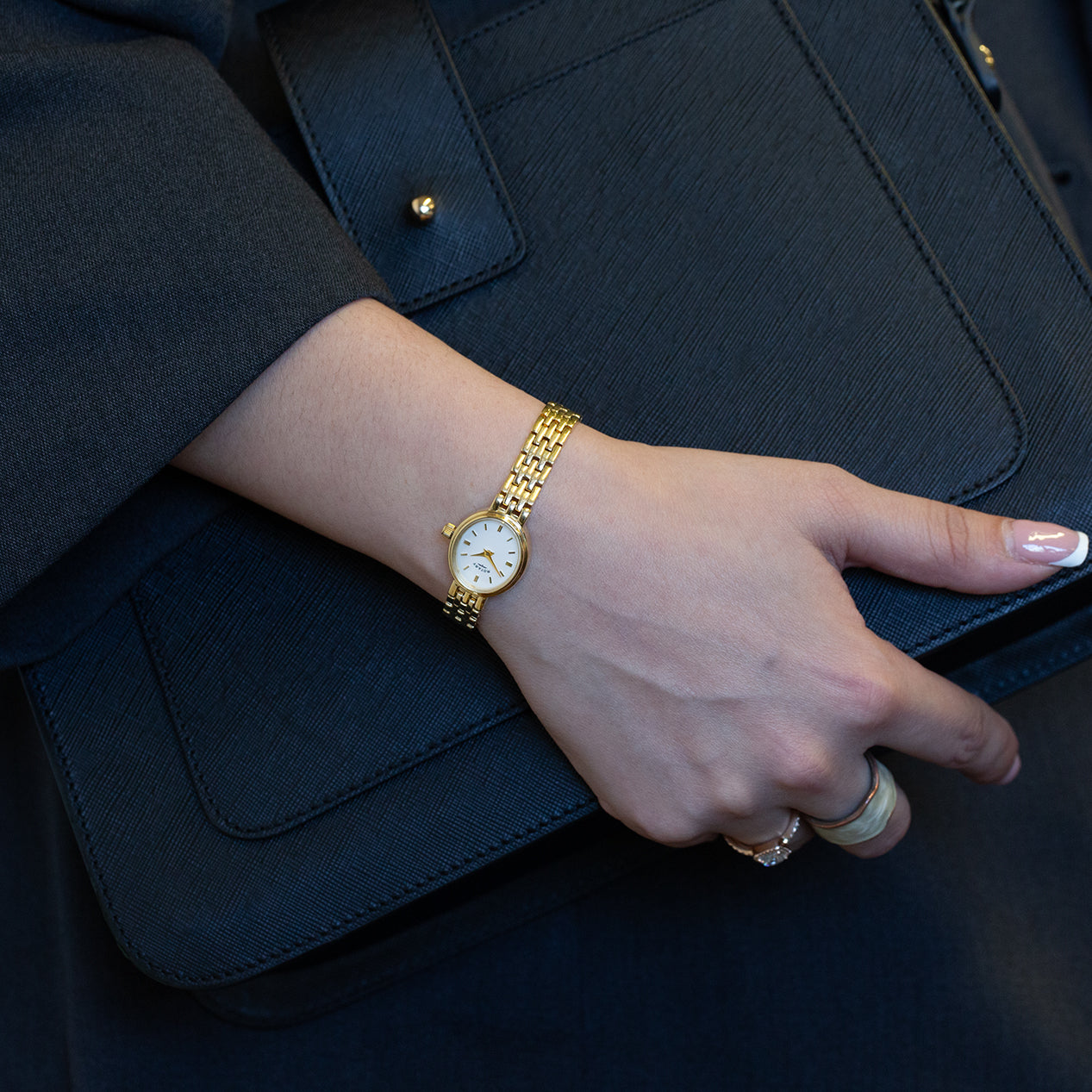 A woman wearing a gold rotary watch holding a black leather handbag