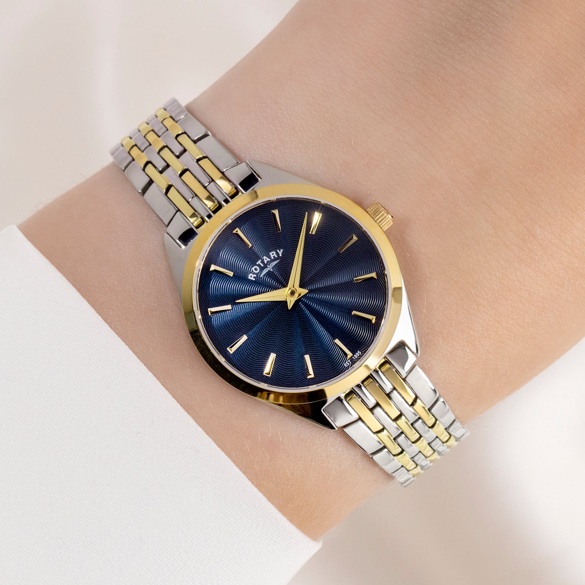 Two-tone watch with blue face and gold accents on a wrist against a light background