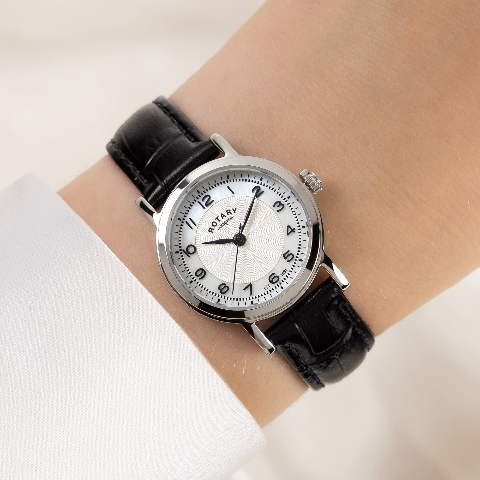 Rotary wristwatch with white face on a wrist against a light background