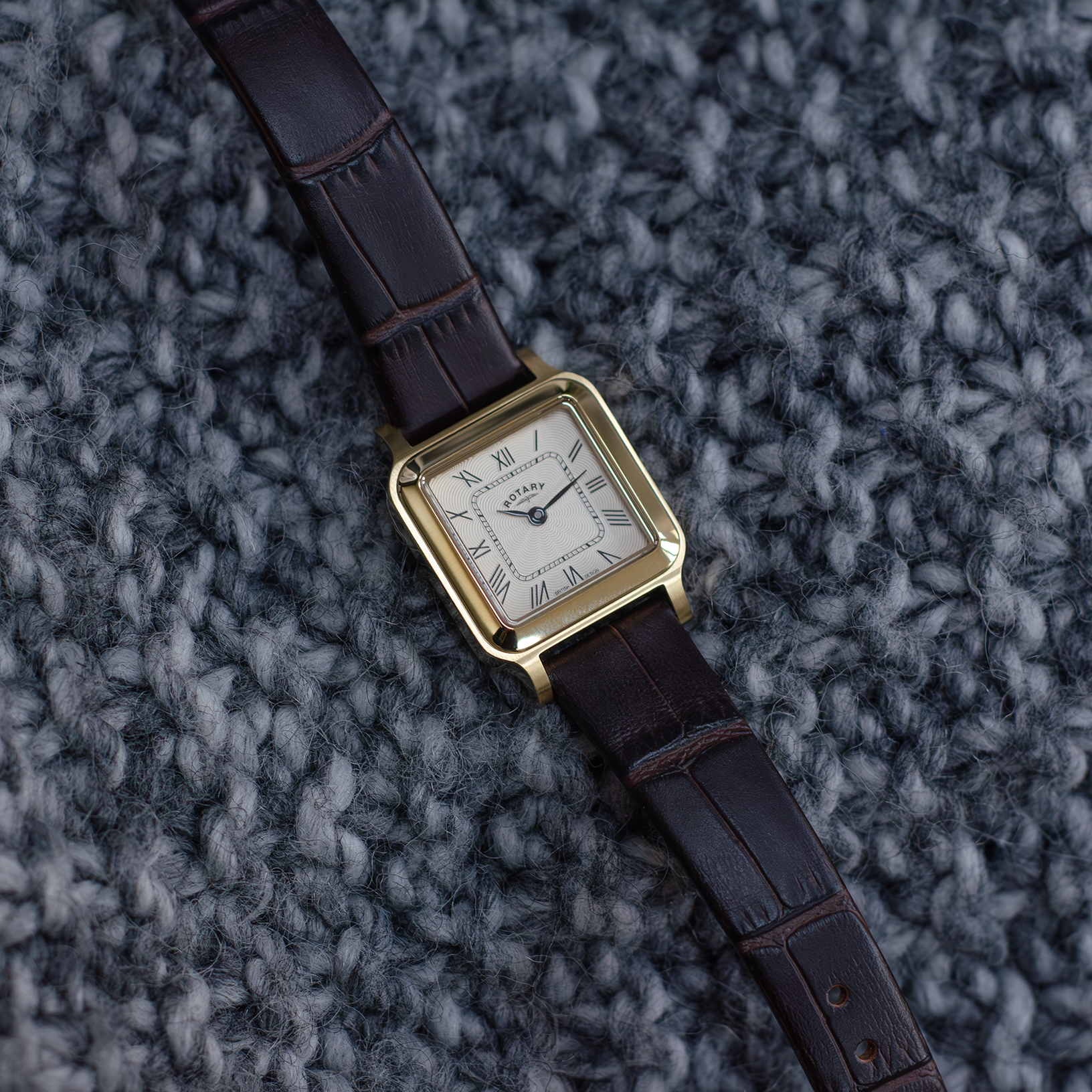 rotary ladies watch in gold with a brown leather strap shot against a grey textured background