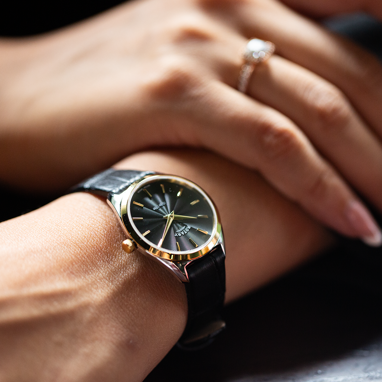 a rotary ladies watch in two tone gold and stainless steel with a black leather strap and black dial being worn by a woman 