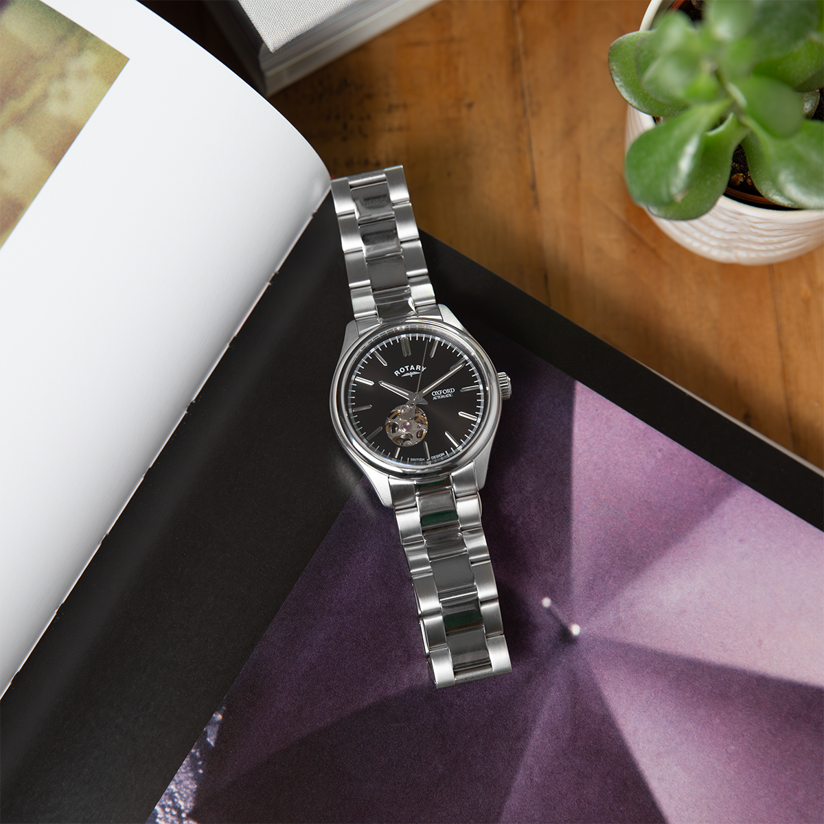 Silver Rotary Oxford watch on a purple surface with a book and plant in the background