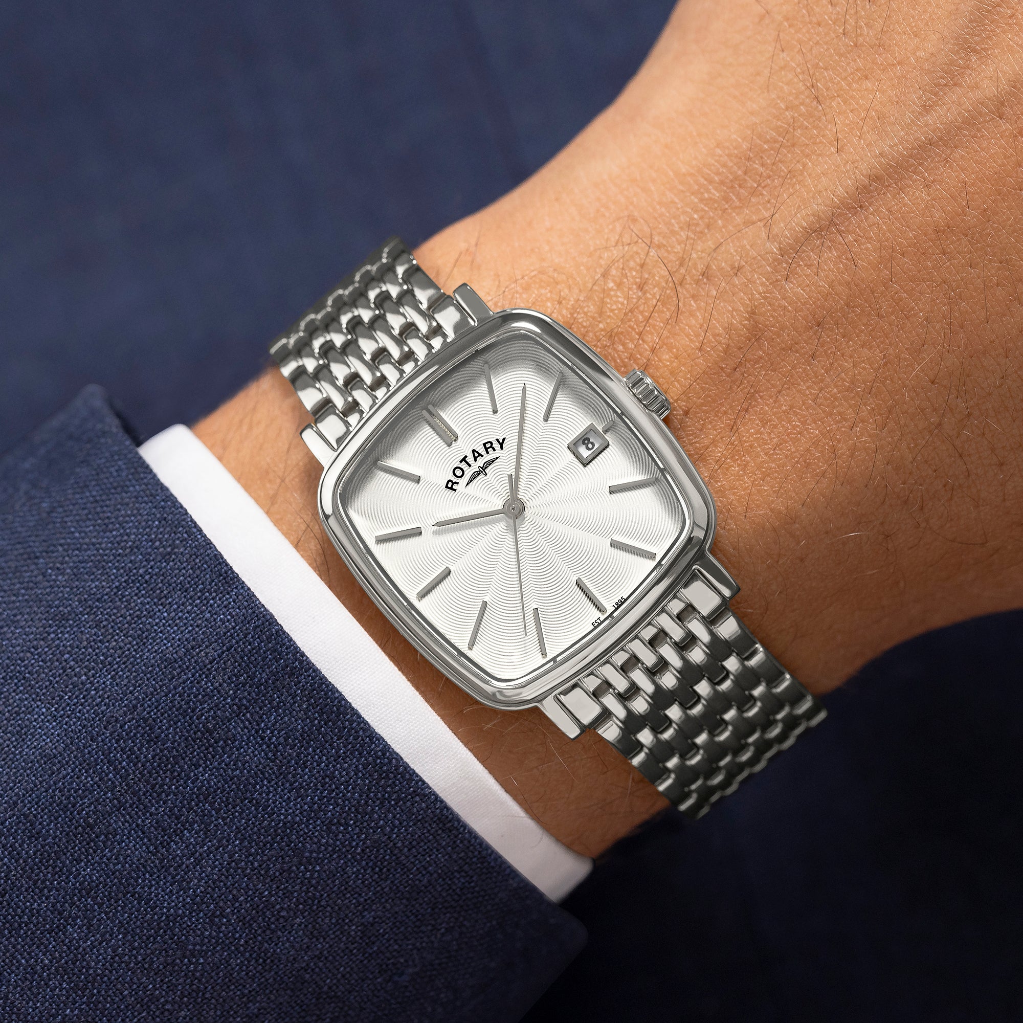 Silver rotary wristwatch worn by a man in a suit.