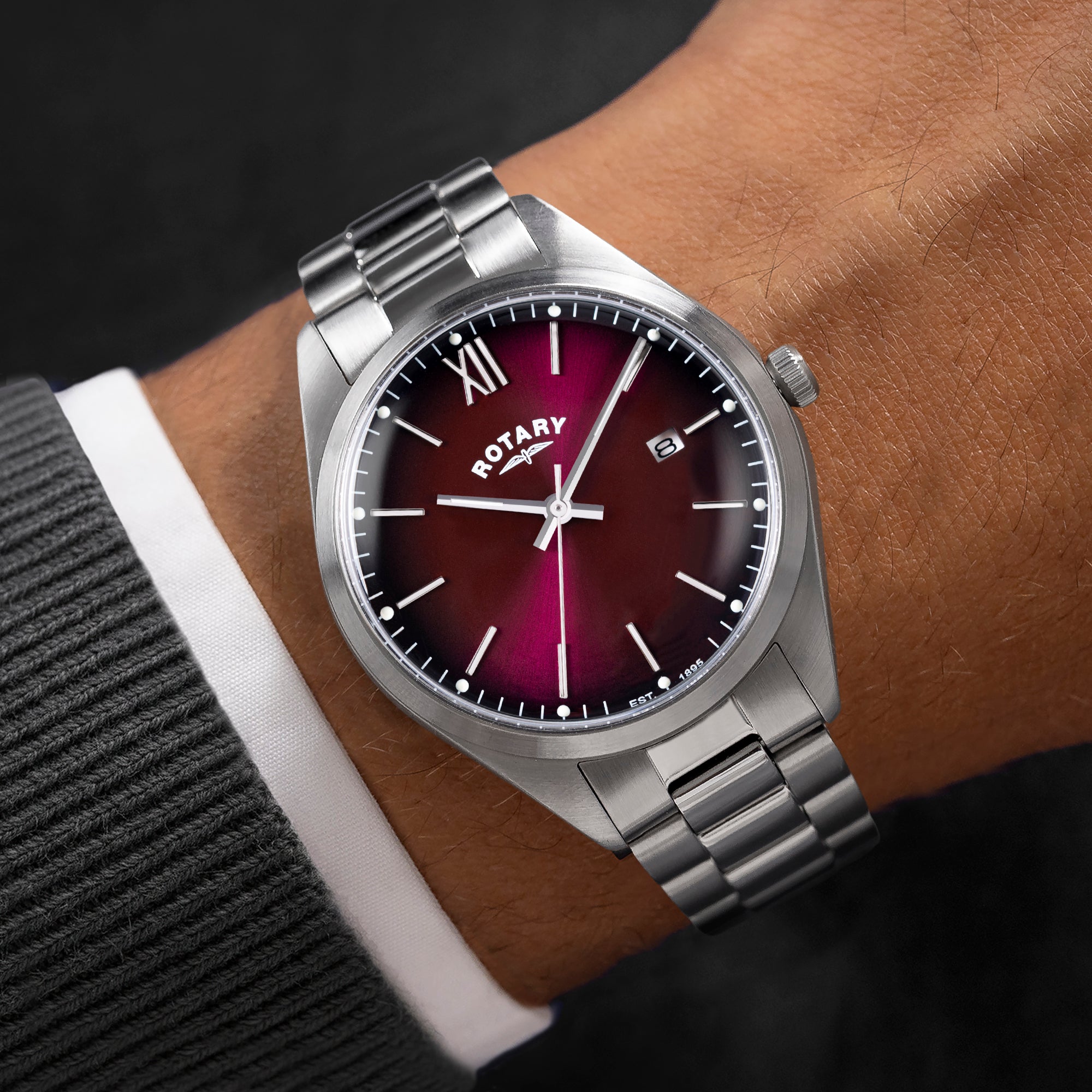 Silver Rotary watch with a maroon dial on a wrist against a dark background
