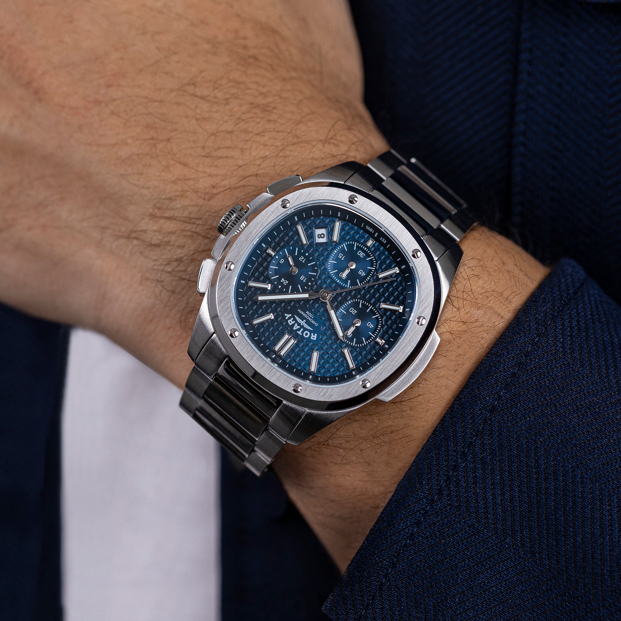 Luxury Rotary Apex100 Chronograph watch with blue face on a person's wrist, wearing a dark suit.