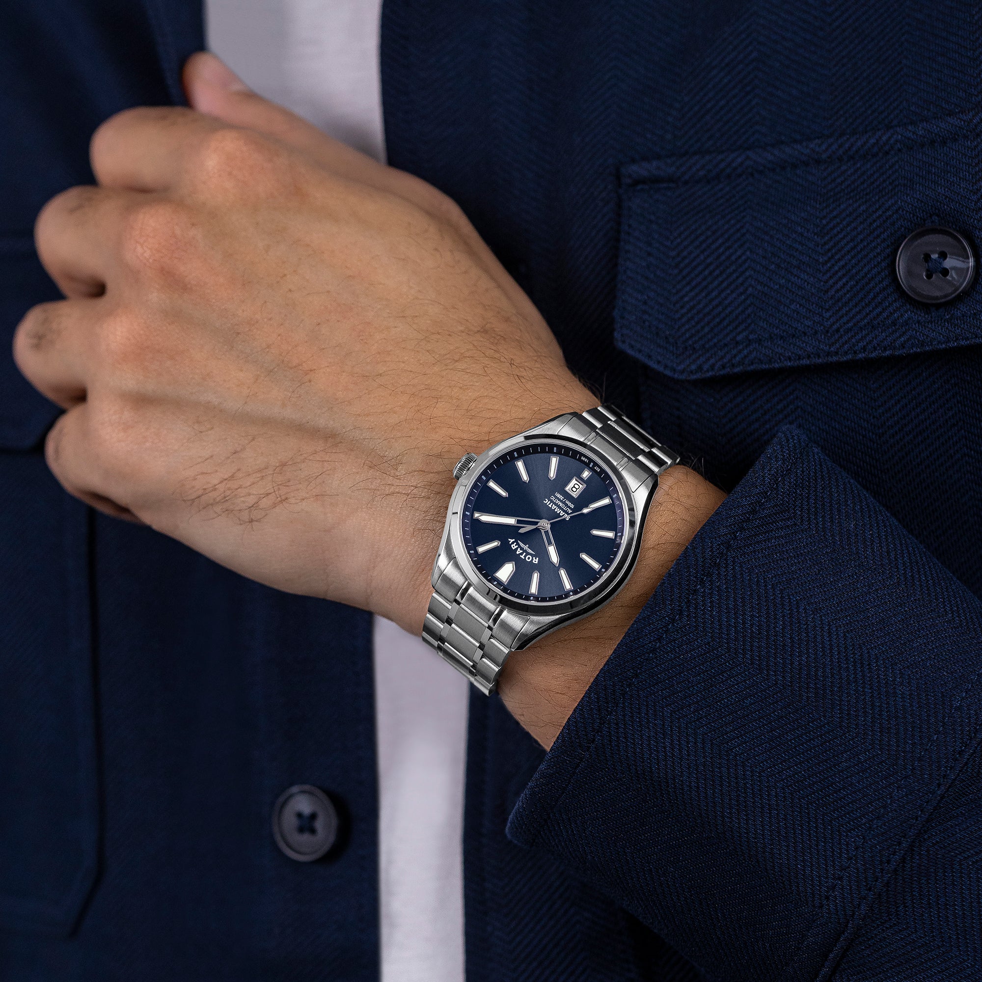 Man wearing a silver Rotary Seamatic 100 watch with a dark face, against a navy suit background