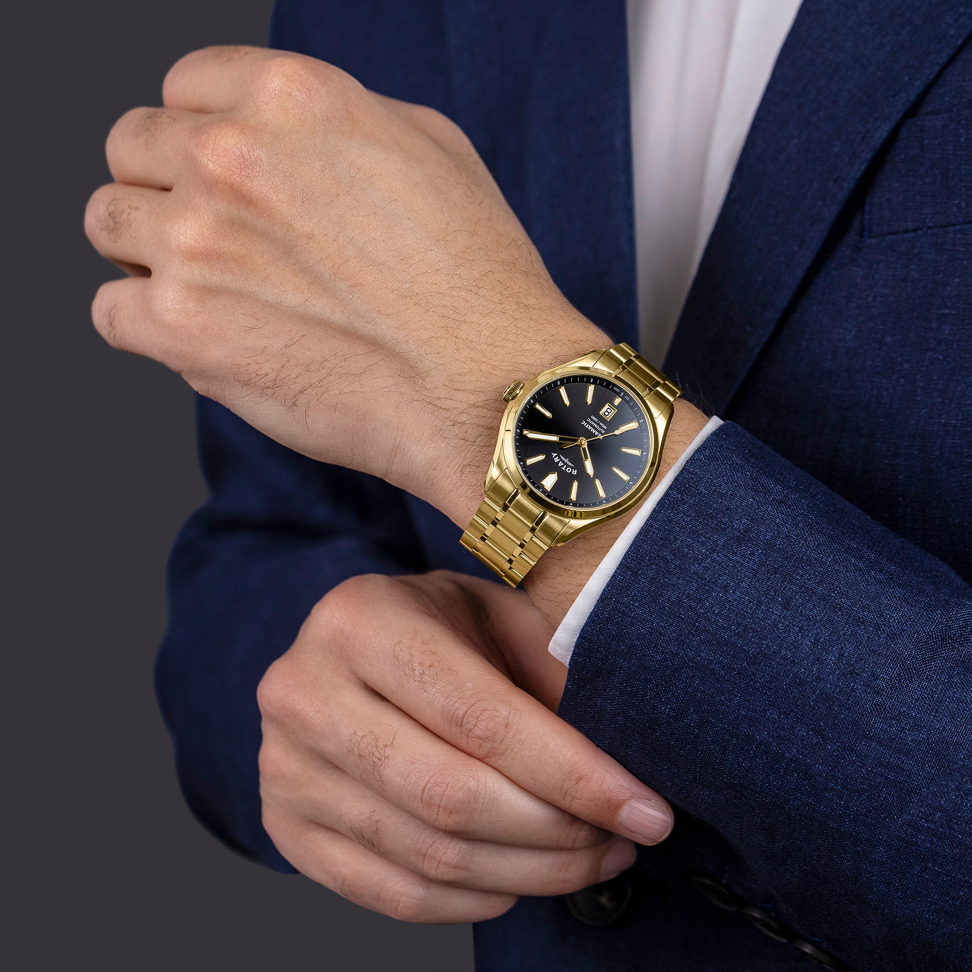 Gold Rotary wristwatch on a man wearing a dark suit against a dark background