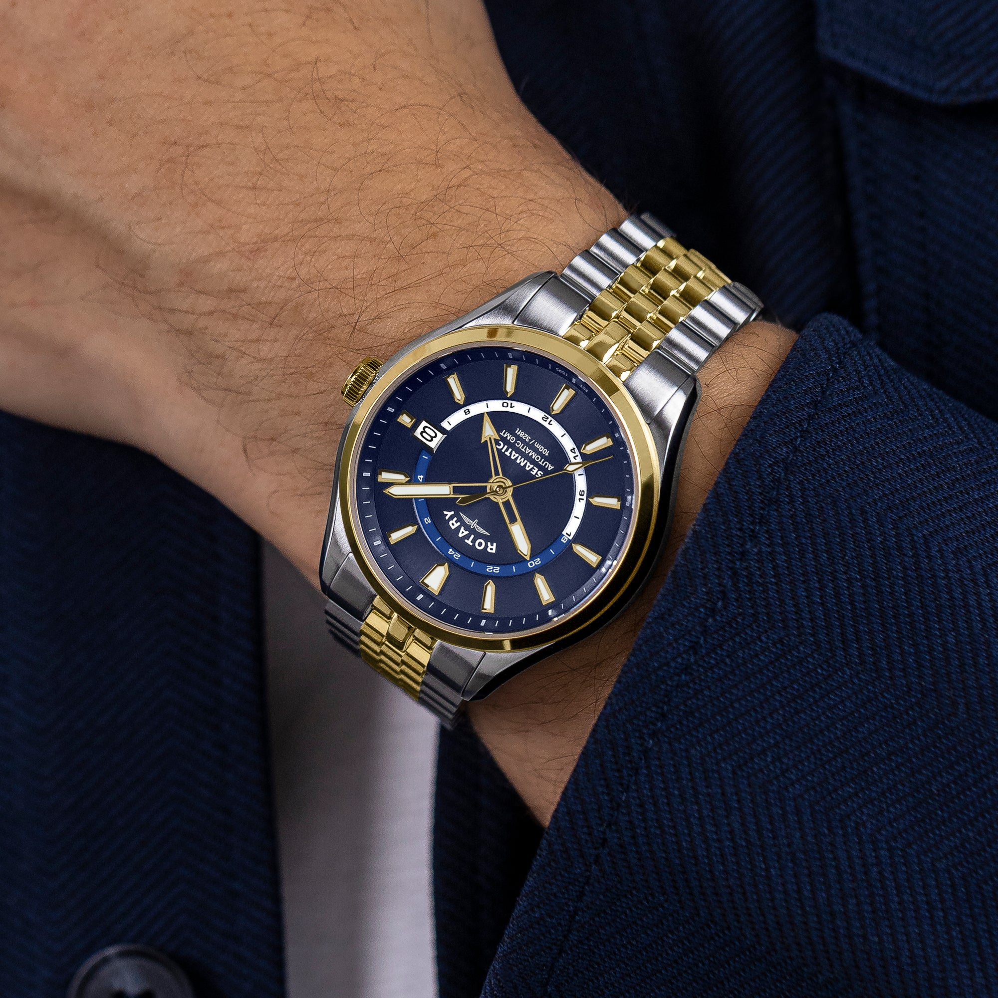 Gold and silver Rotary Seamatic 100 GMT watch with blue face on a wrist, wearing a dark suit