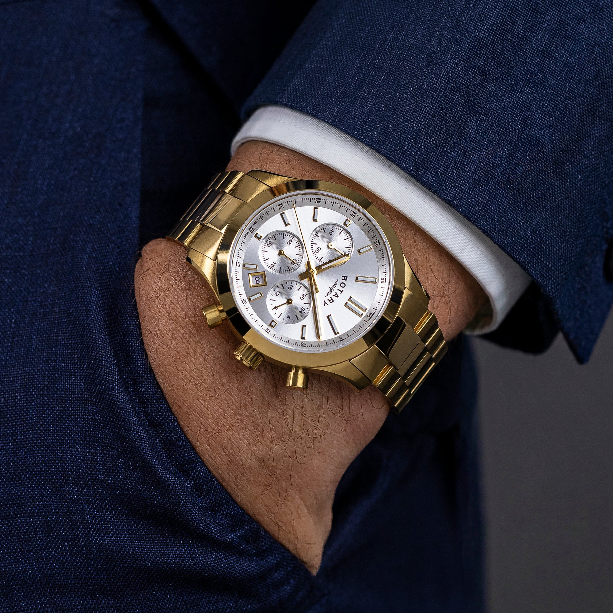 Gold Rotary Heritage Chronograph wristwatch on a person's wrist with a dark suit and white shirt.