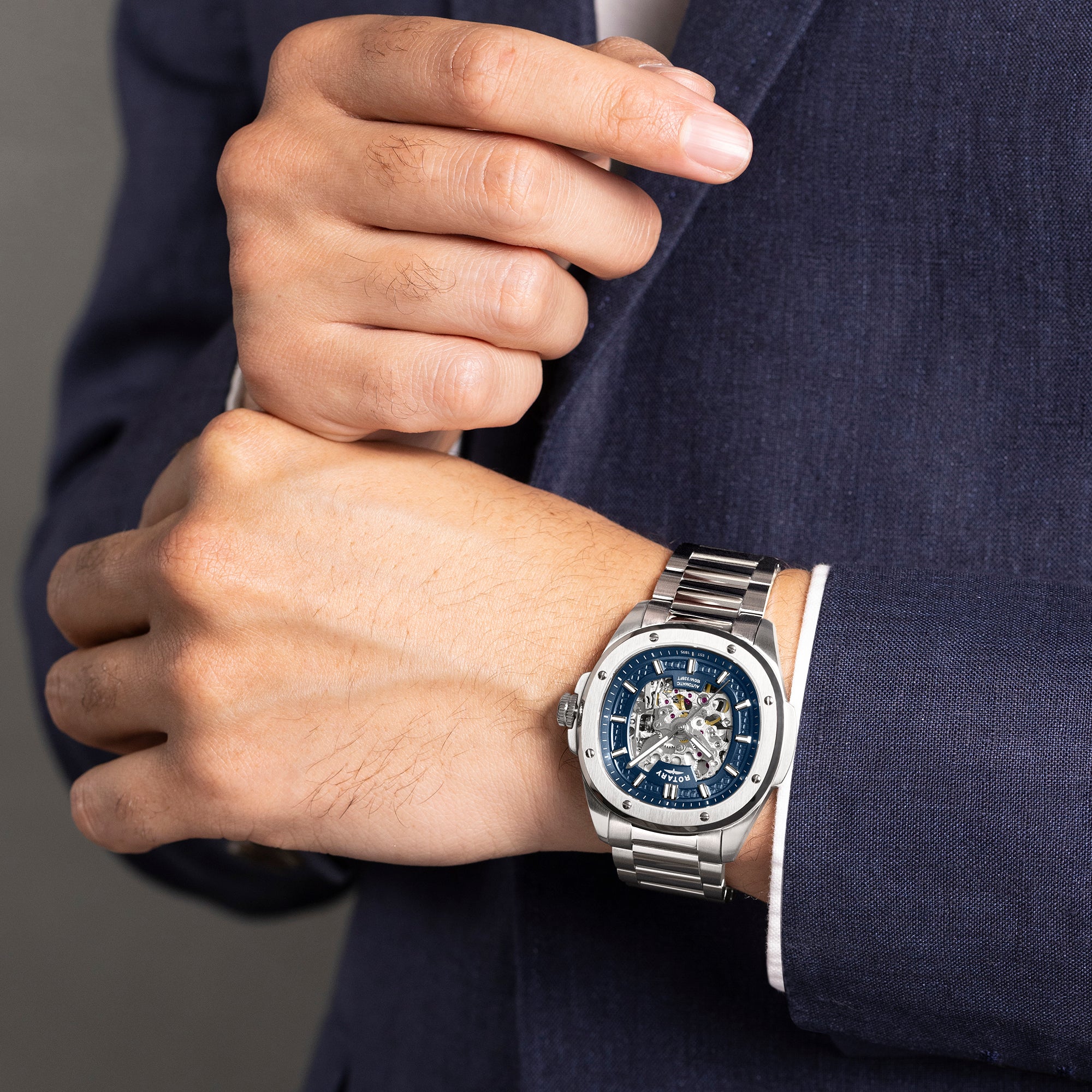Man wearing a silver Rotary watch with a blue face on a dark suit background
