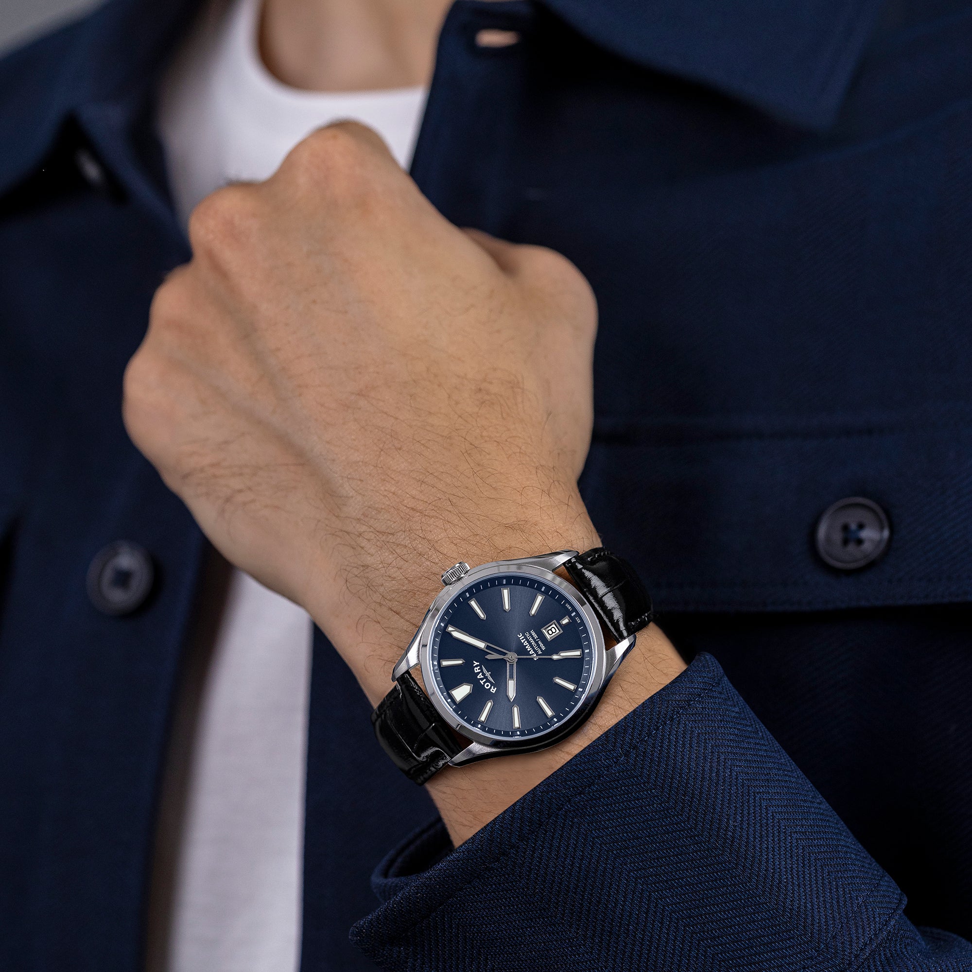 Man wearing a Seamatic 100 watch with a dark blue face and black strap, against a blurred background.