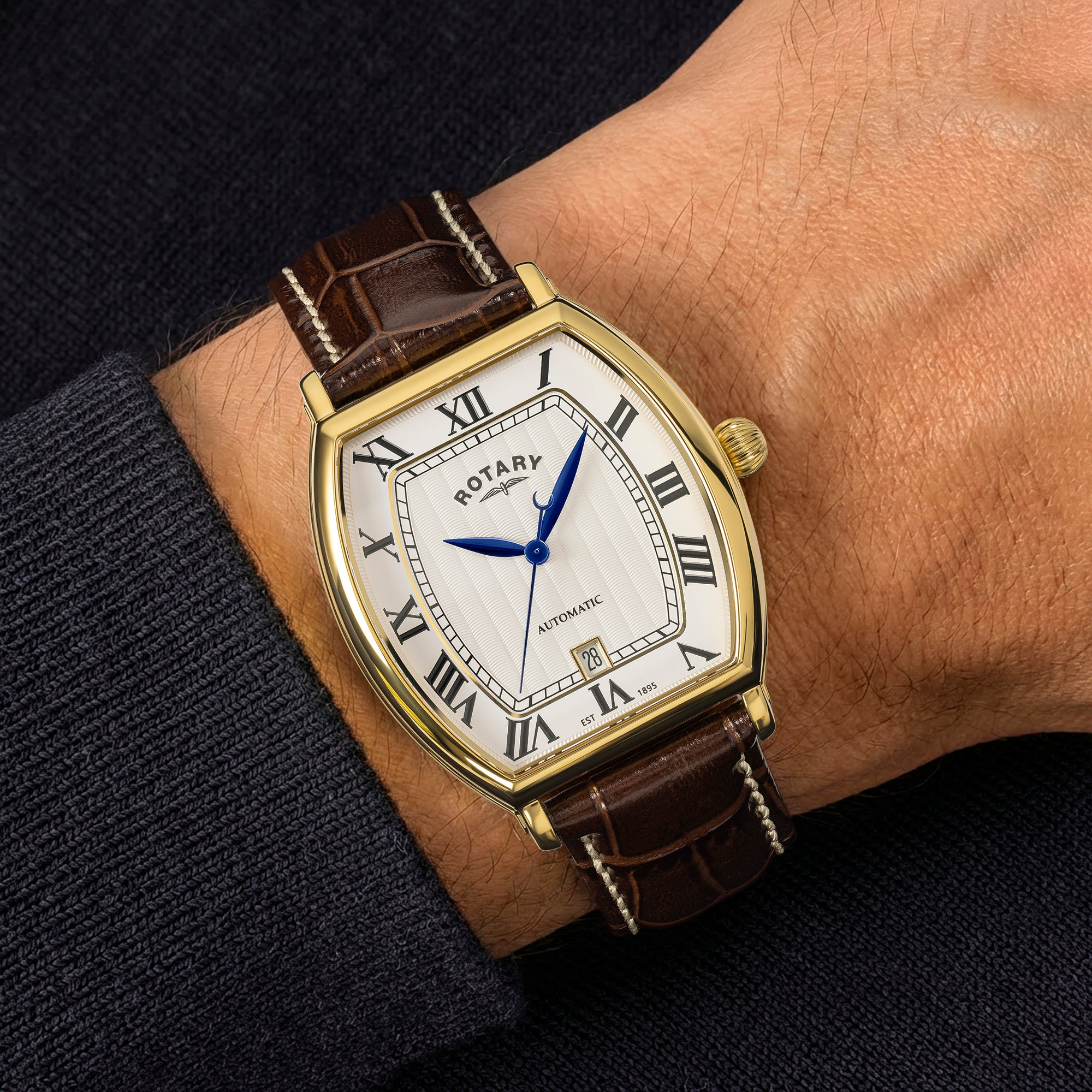 Rotary 1895 automatic tonneau watch with brown leather strap on a wrist against a dark background