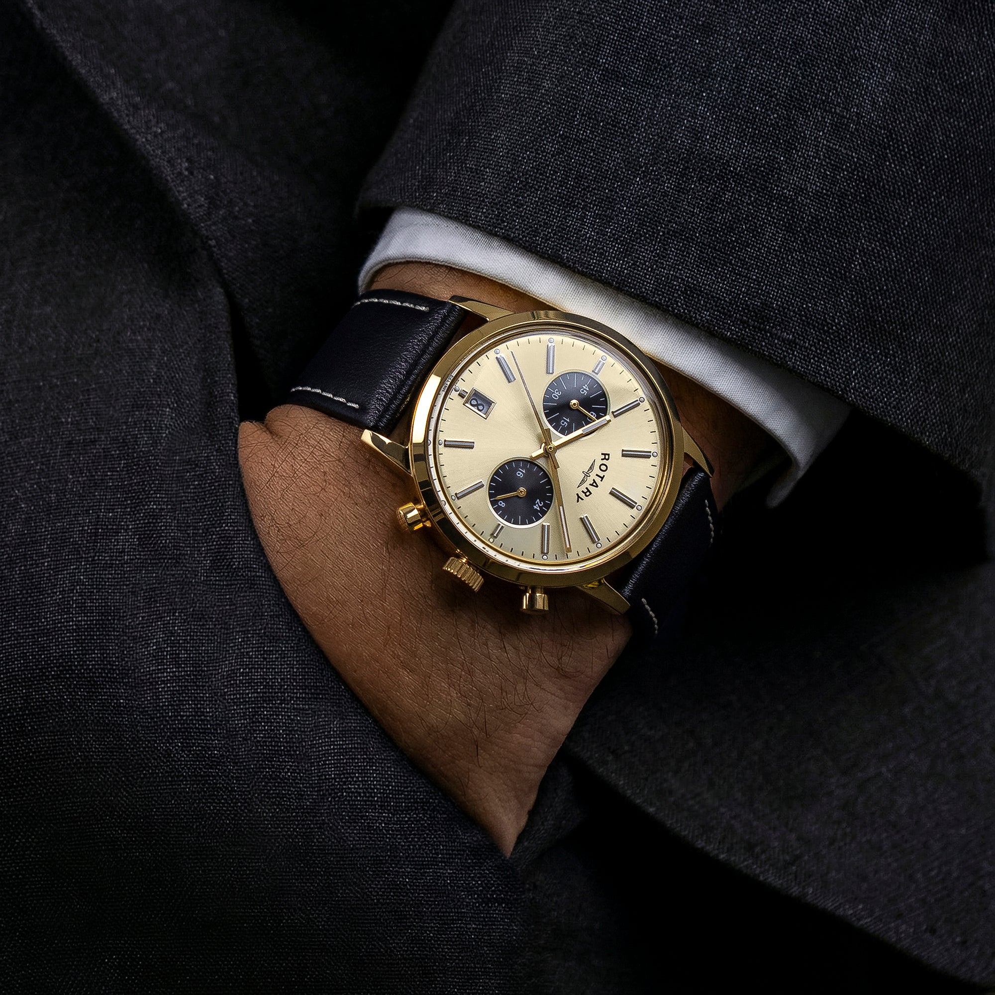 Luxury Rotary 1895 Chronograph watch with gold case and black leather strap worn on a dark suit sleeve.
