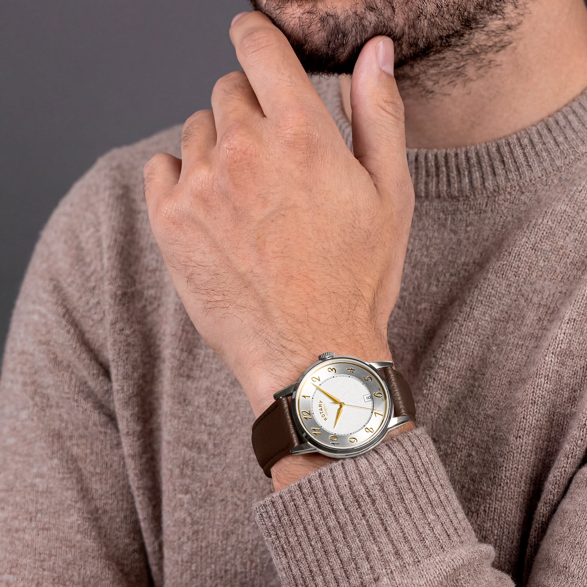 Man wearing a brown sweater and a Rotary watch with a brown leather strap on a neutral background