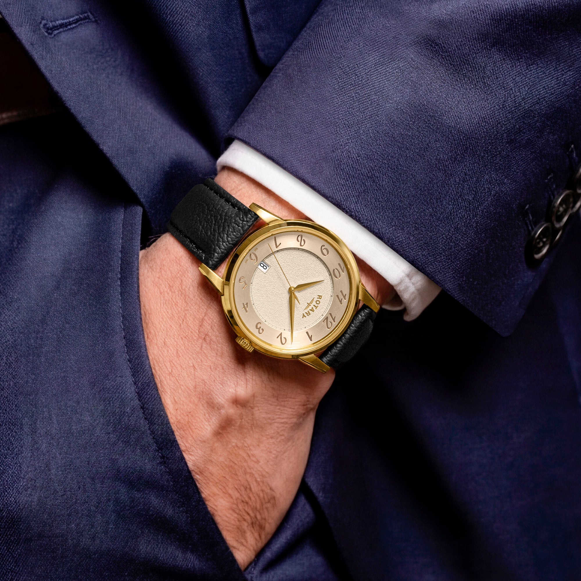 Gold Rotary watch with black leather strap on a man wearing a navy suit and white shirt.