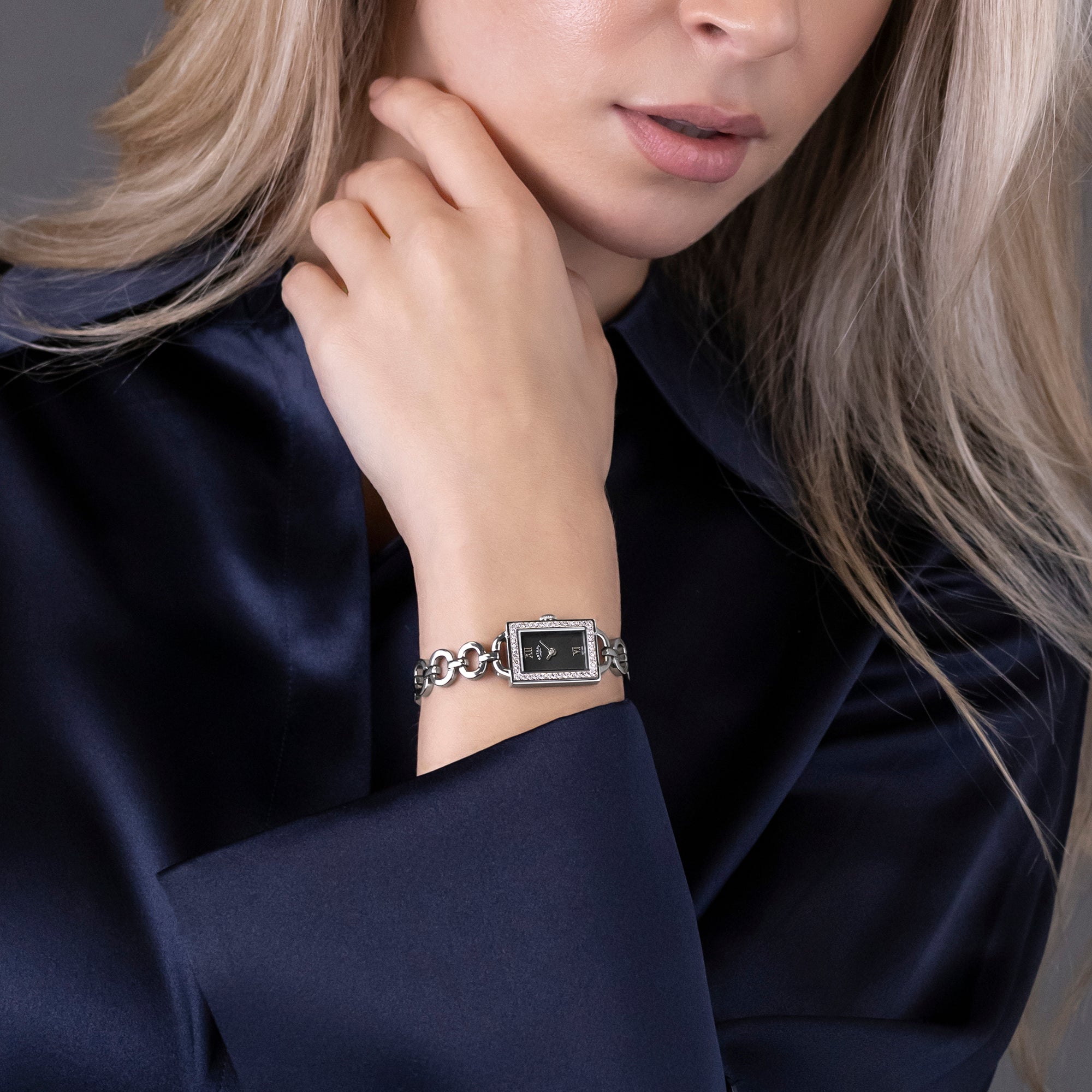Woman wearing a silver bracelet Rotary watch with a dark dial on a dark blue garment.
