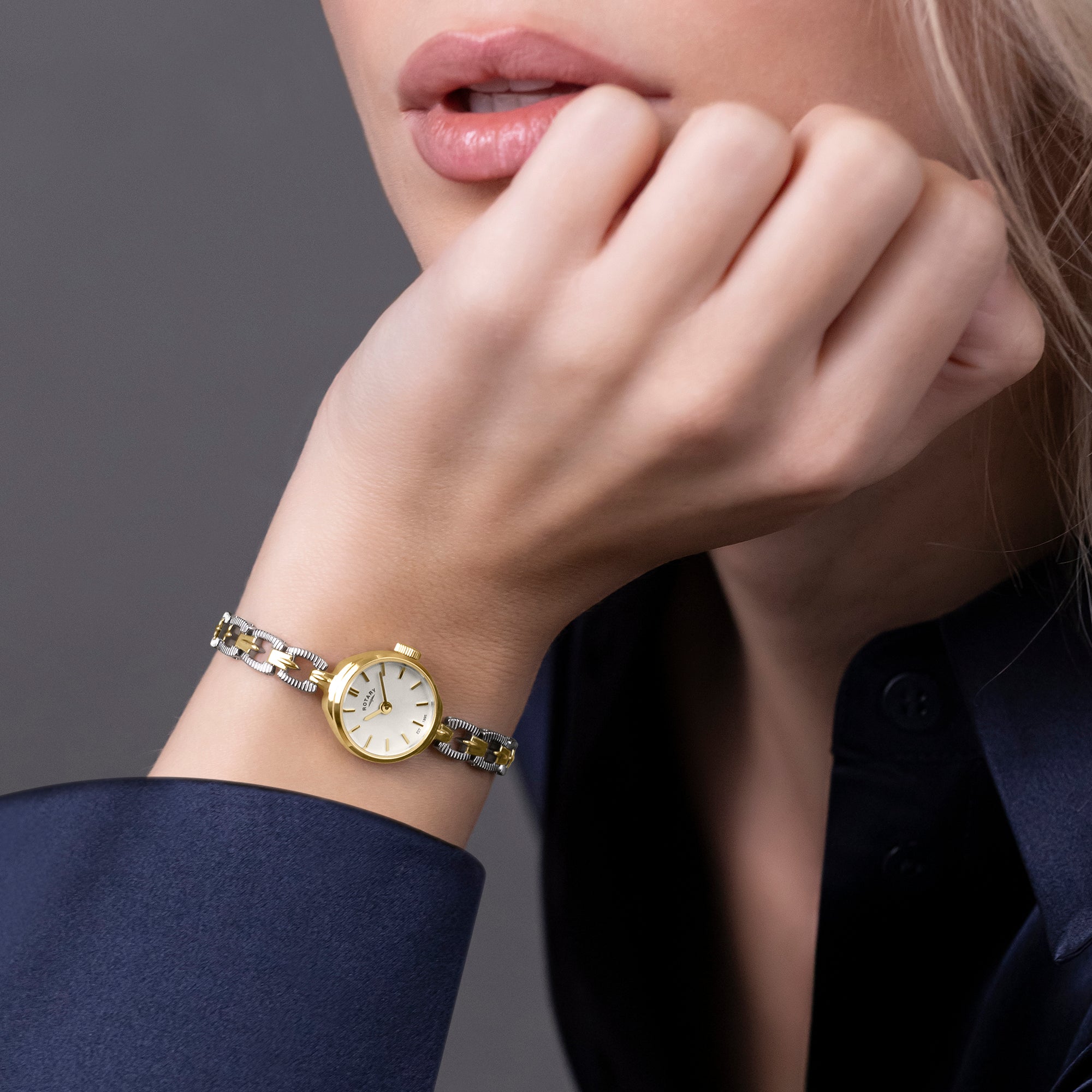 Close-up of a woman wearing a gold and silver Rotary watch on a dark background