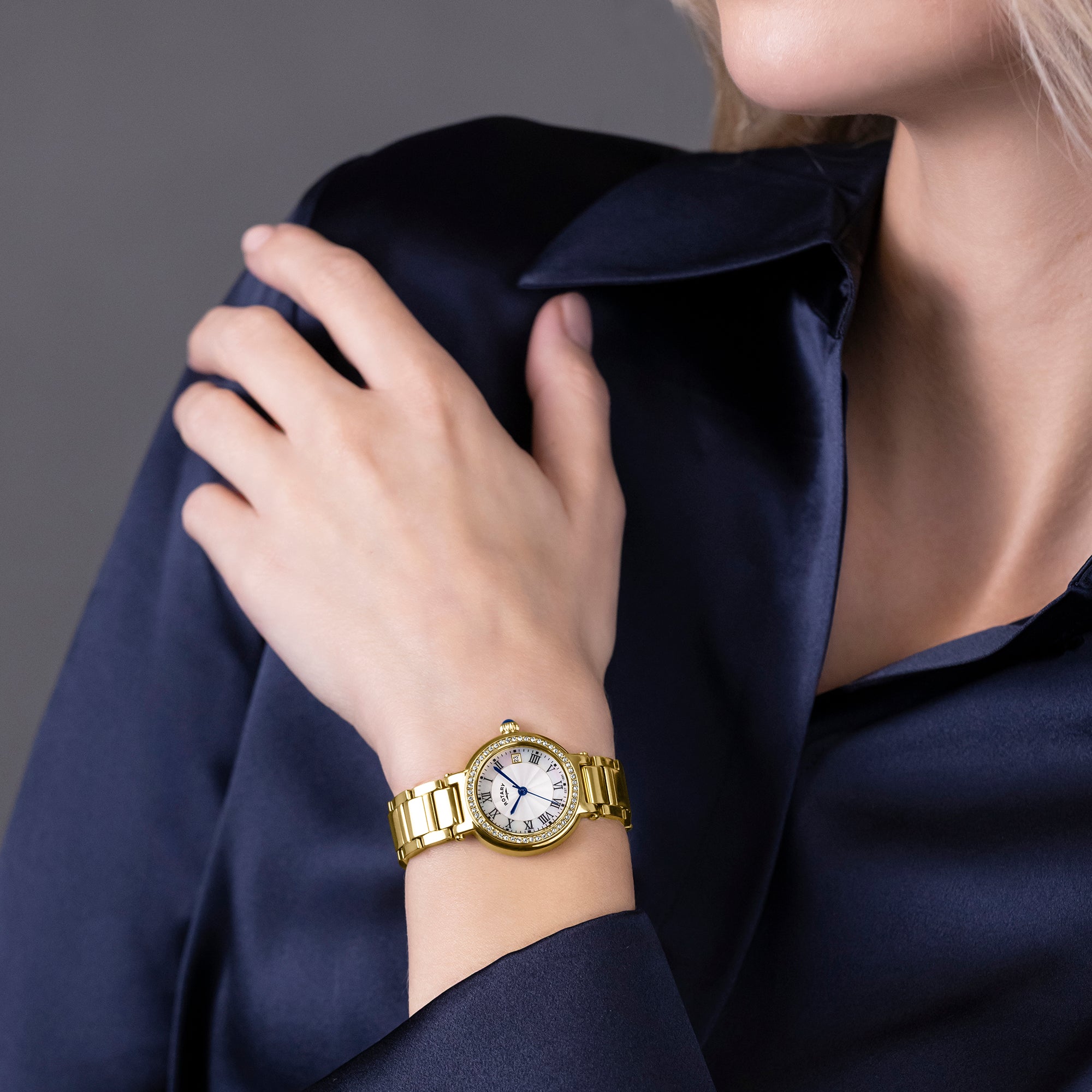 Gold Rotary watch on a woman wearing a dark blue shirt against a gray background