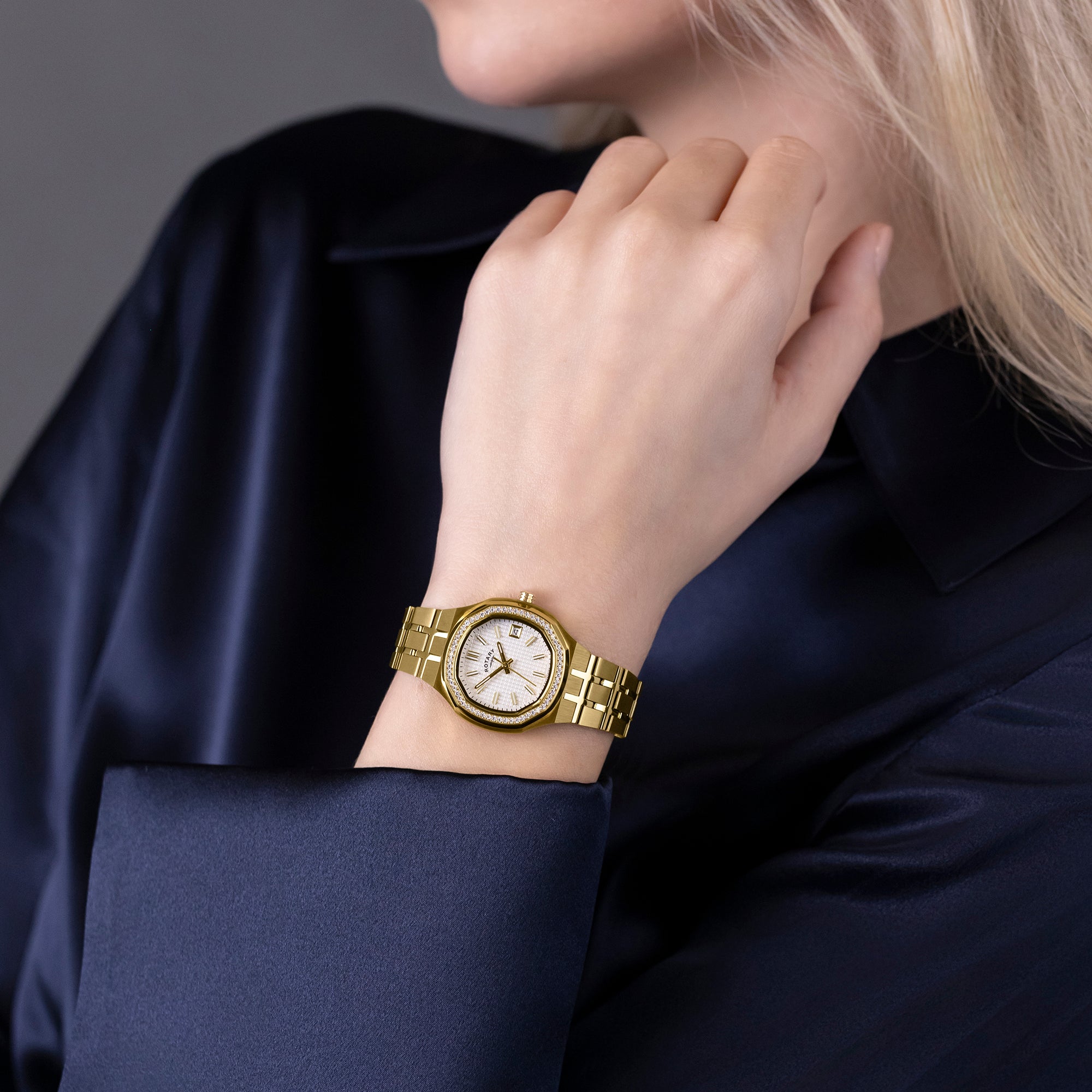 Gold Rotary Brilliance watch on a woman's wrist with a dark blue fabric background