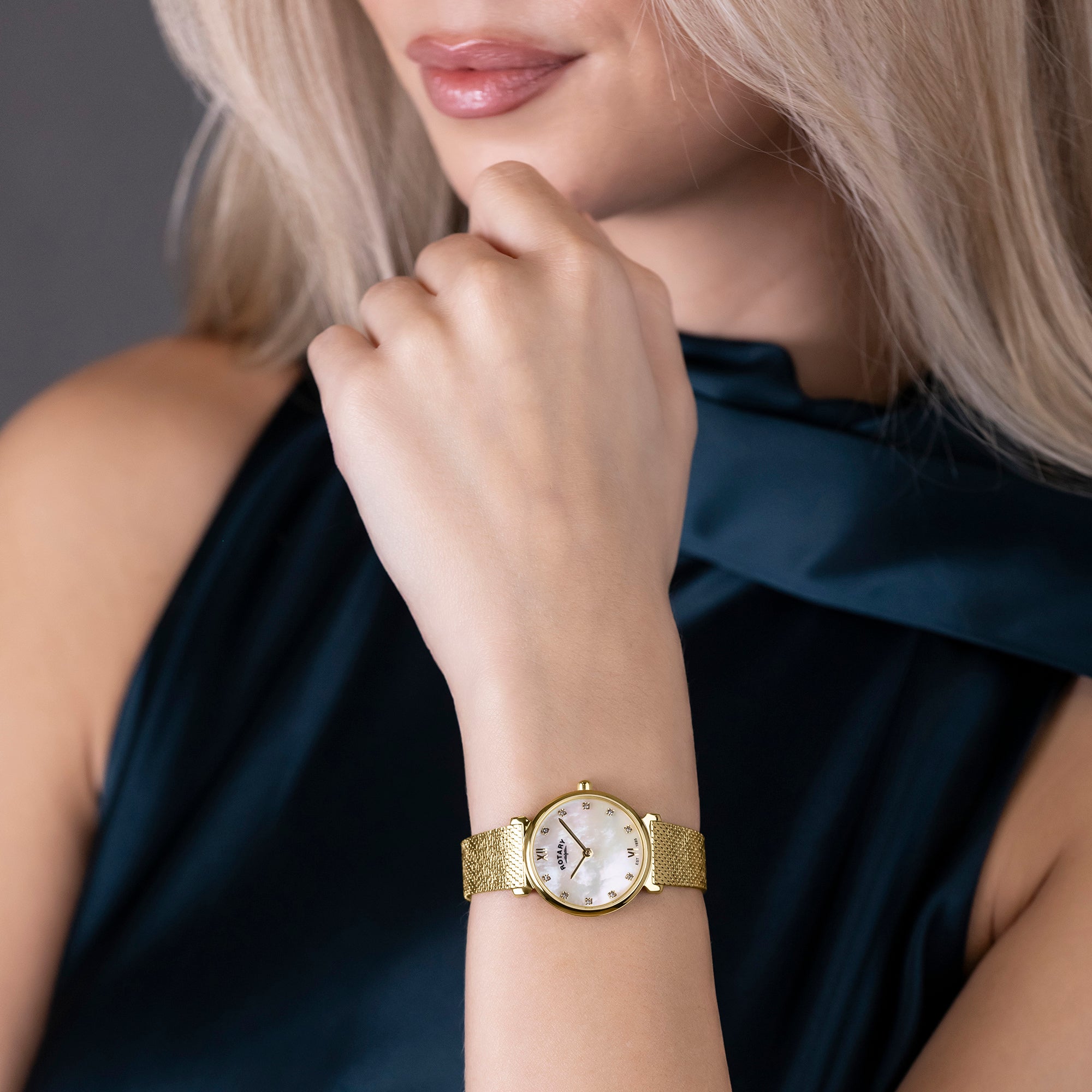 Woman wearing a gold Rotary 1895 watch on a dark background