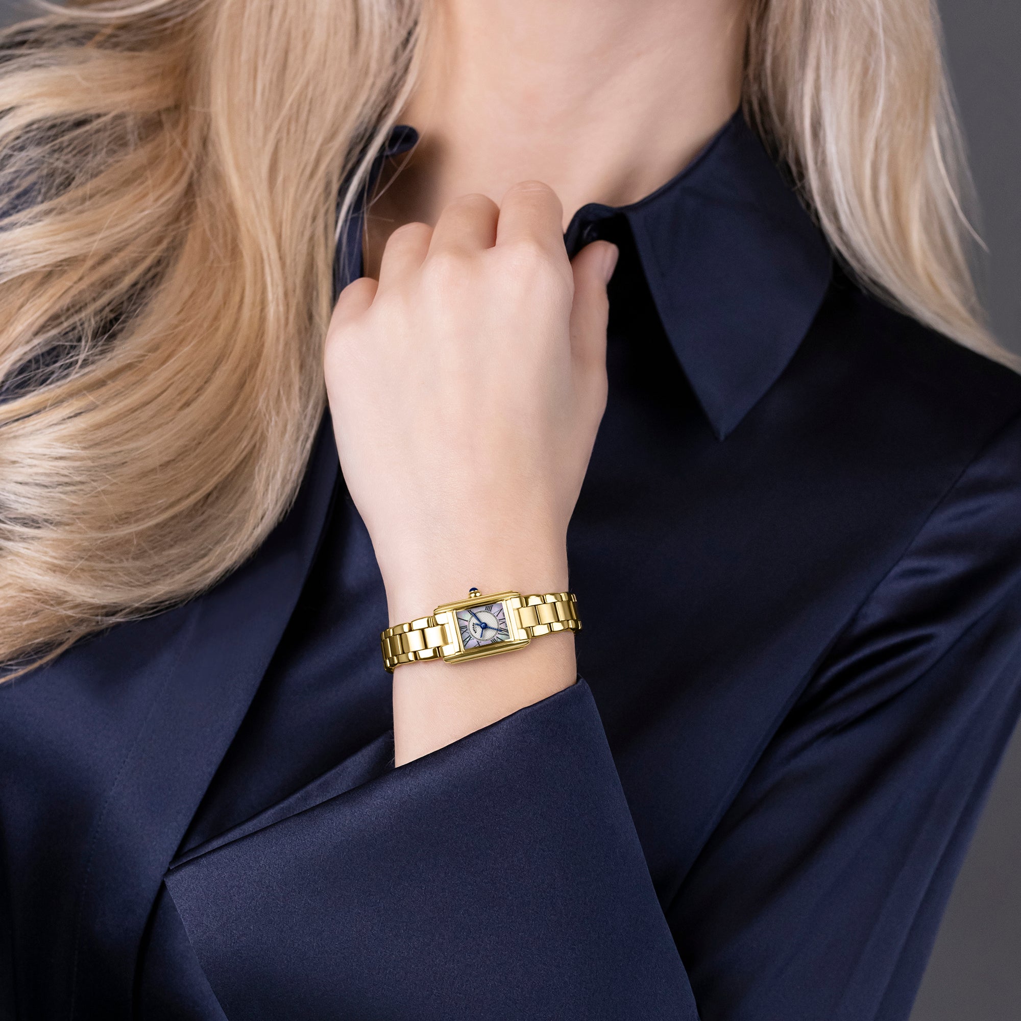 Woman wearing a gold Rotary bracelet watch with a clear gemstone on a dark background