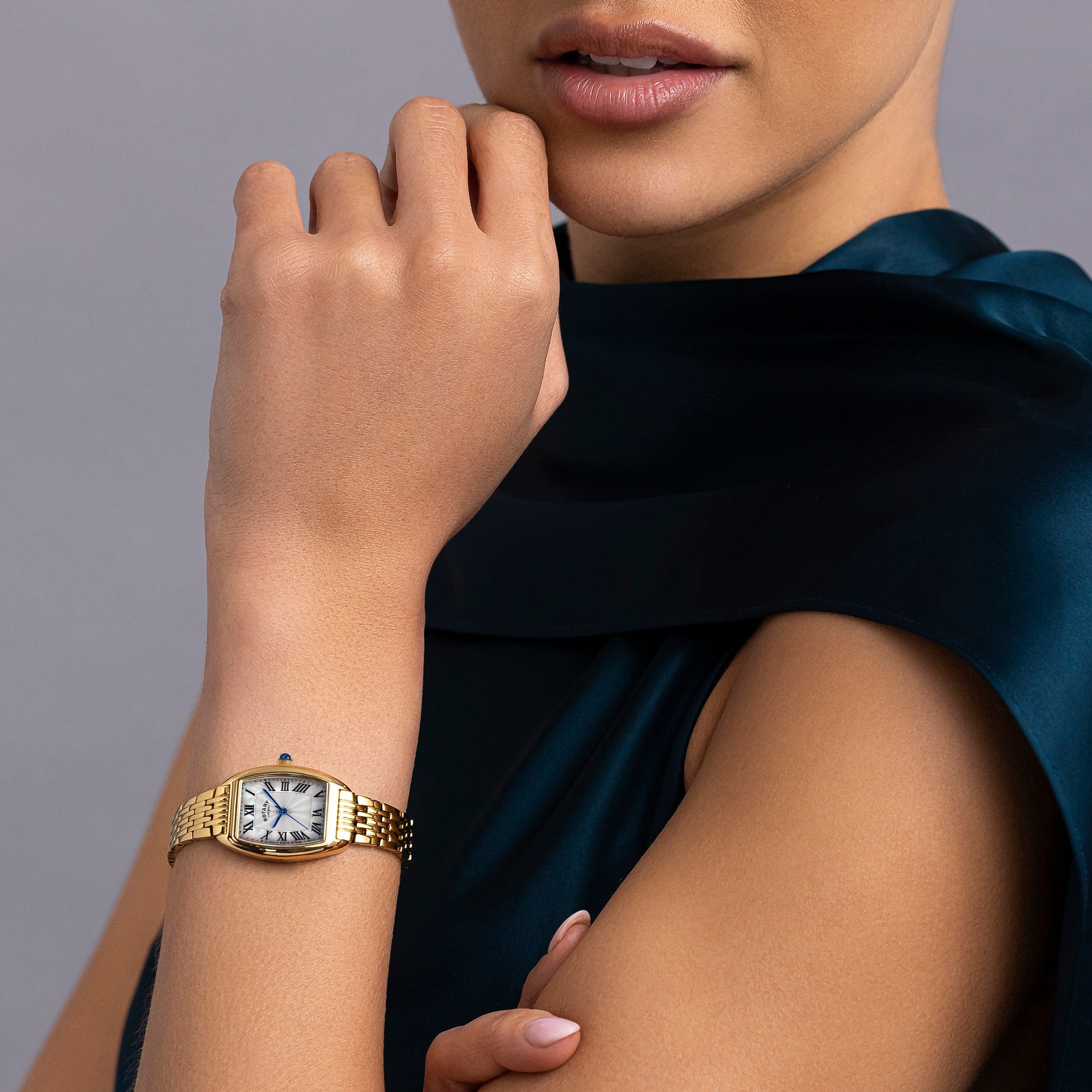 Gold Rotary 1895 Tonneau wristwatch on a person's wrist with a neutral background