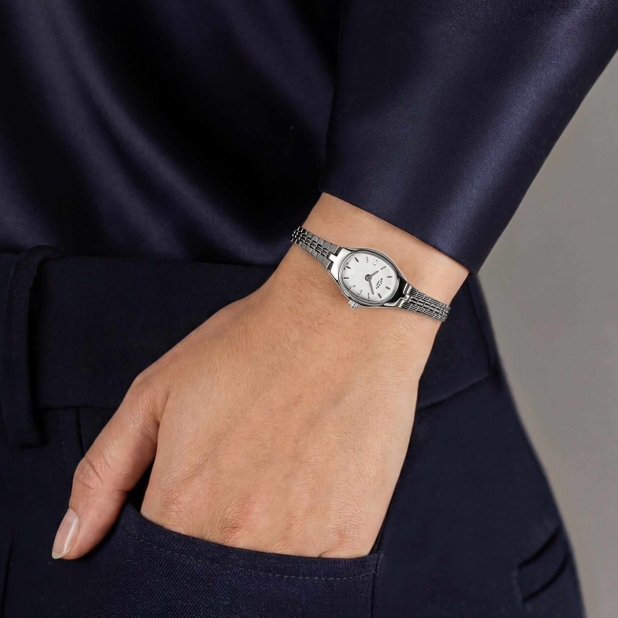 Hand wearing a women's silver Rotary watch on a plain background